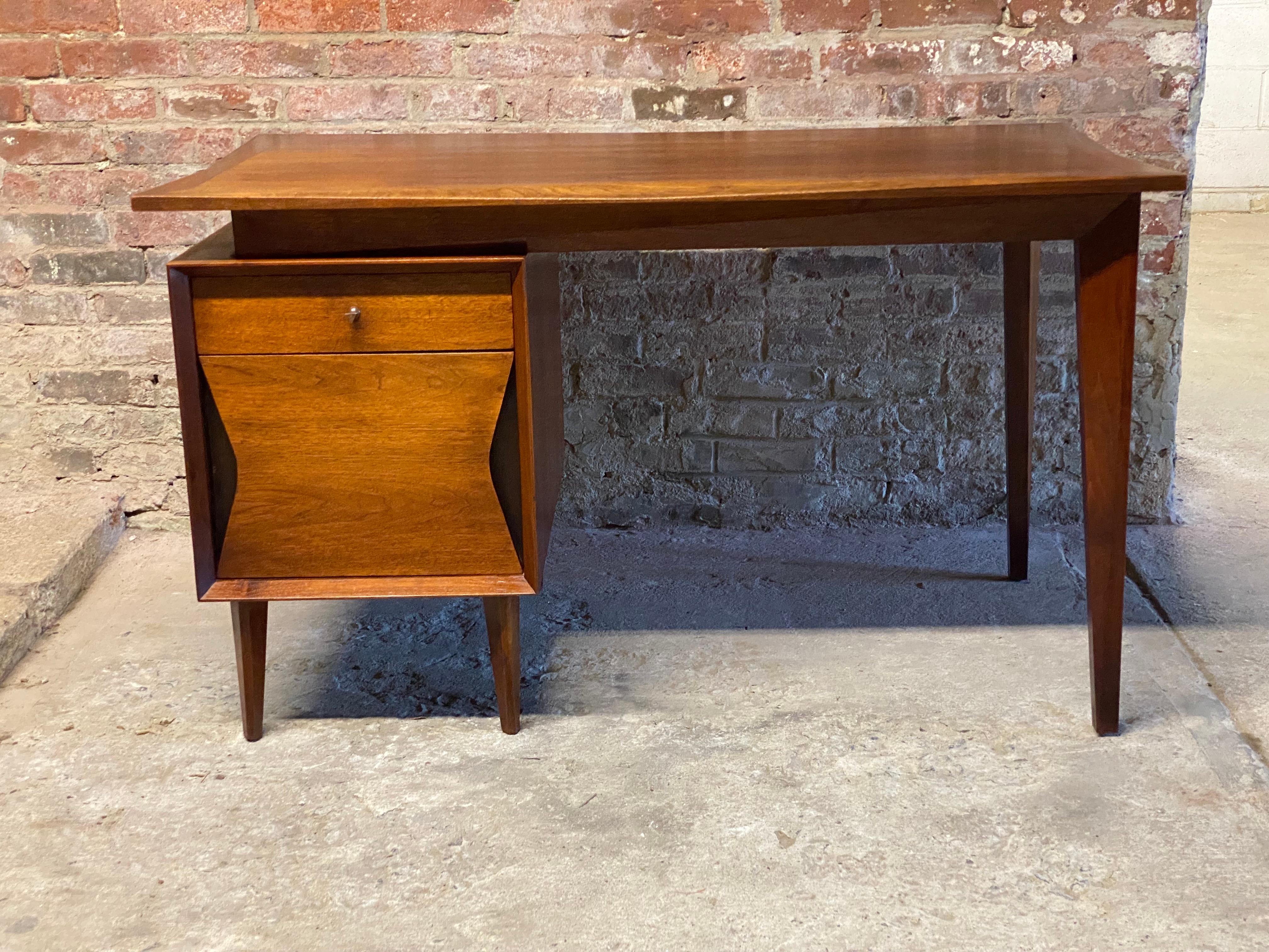 Roomy and commodious Walnut desk featuring a slightly beveled edge and apron, faceted tapered legs and ebonized accent detail surrounding the bottom drawer. The bottom drawer can be used for deep storage or hanging files. Circa 1960. Finished on all