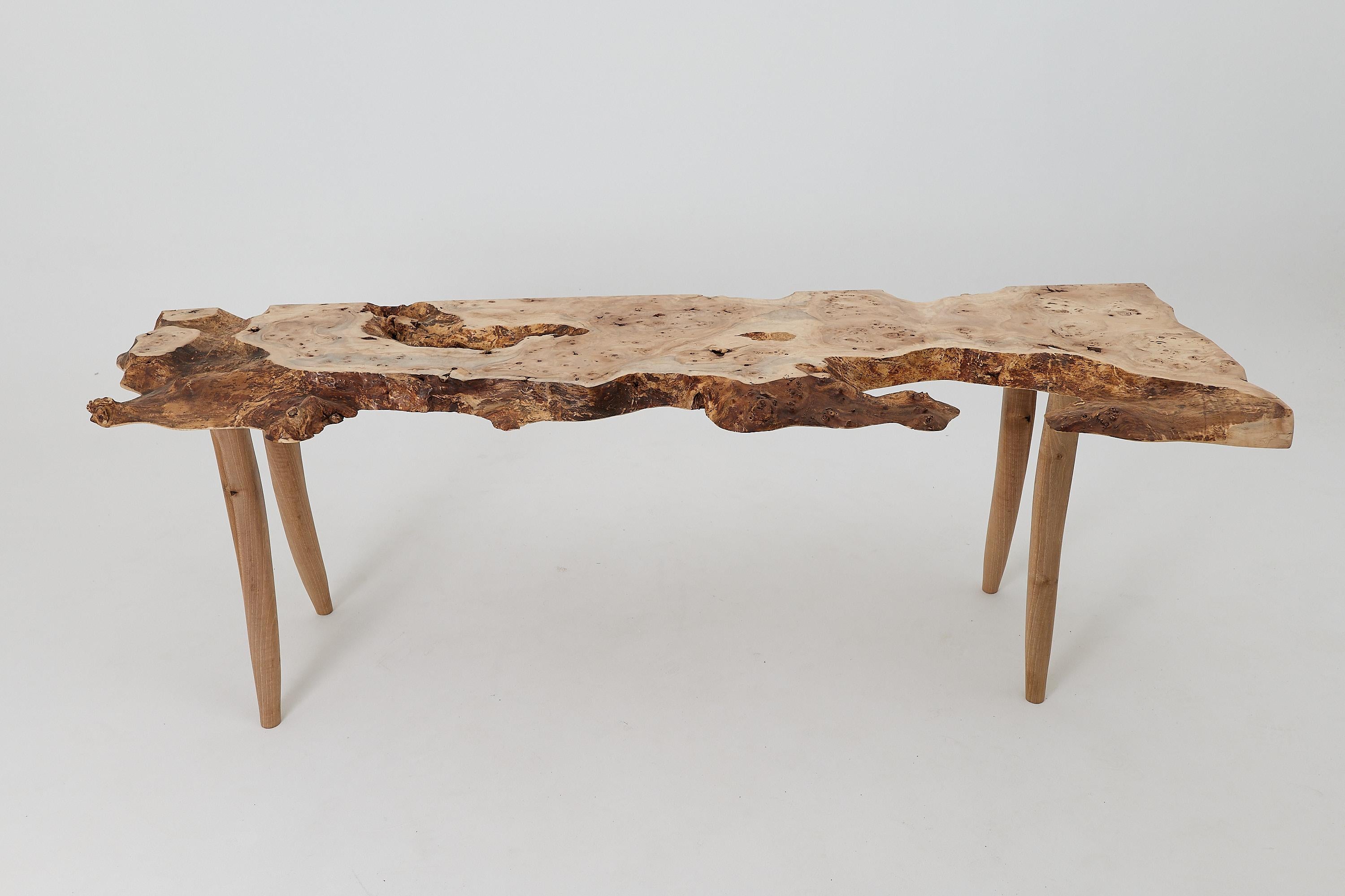 Cette table console captivante est une pièce unique, célébrant la beauté sauvage d'une plaque de loupe de bois dur massif. Sa forme est une étude de contrastes. Le plateau brut à arêtes vives est un paysage de contours naturels et de grains
