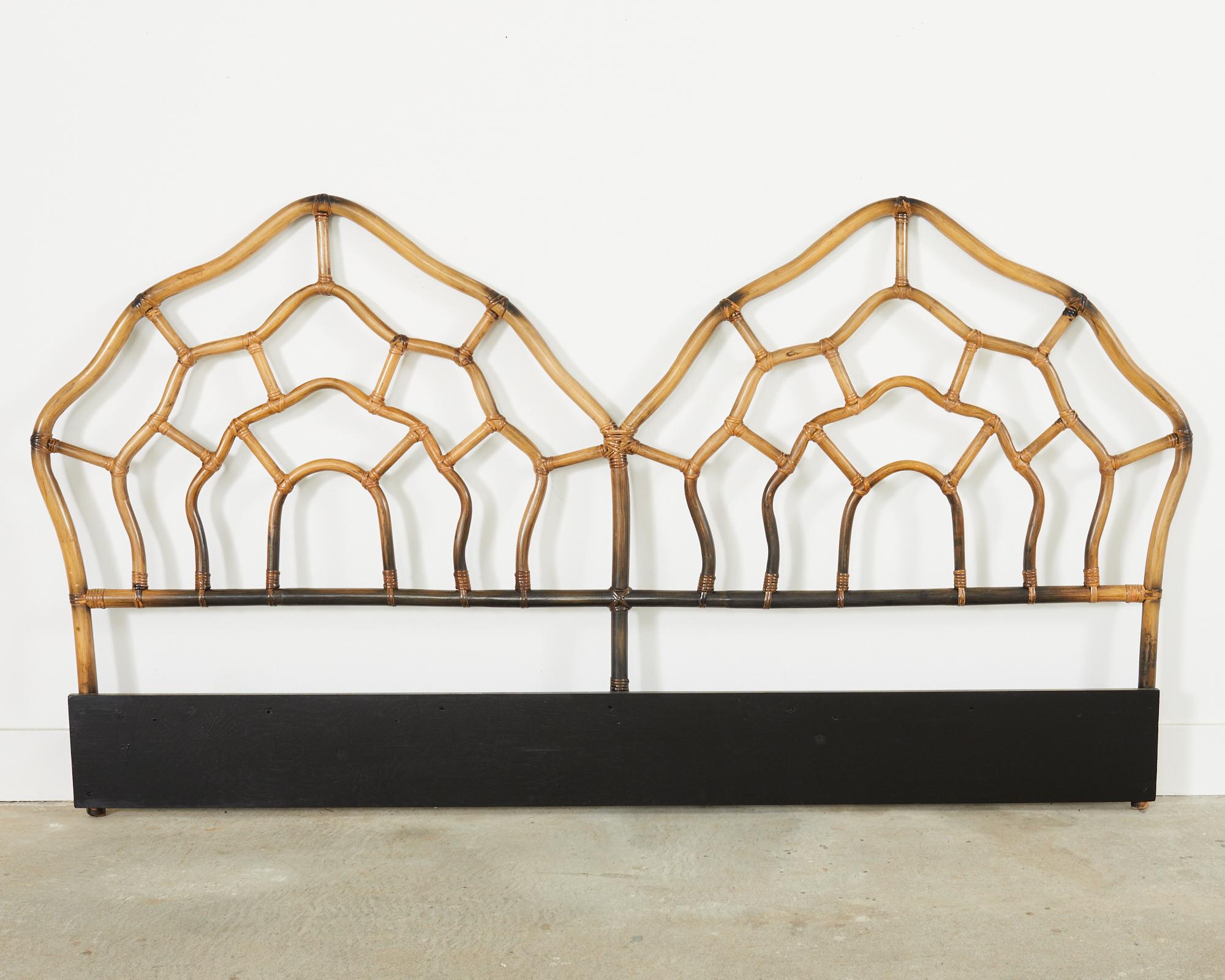 Monumental double headboard measuring 7 feet wide constructed from bent rattan featuring a faux-scorched bamboo style finish. Double humped crest with an open fretwork of conforming serpentine shapes. Made in the California coastal organic modern