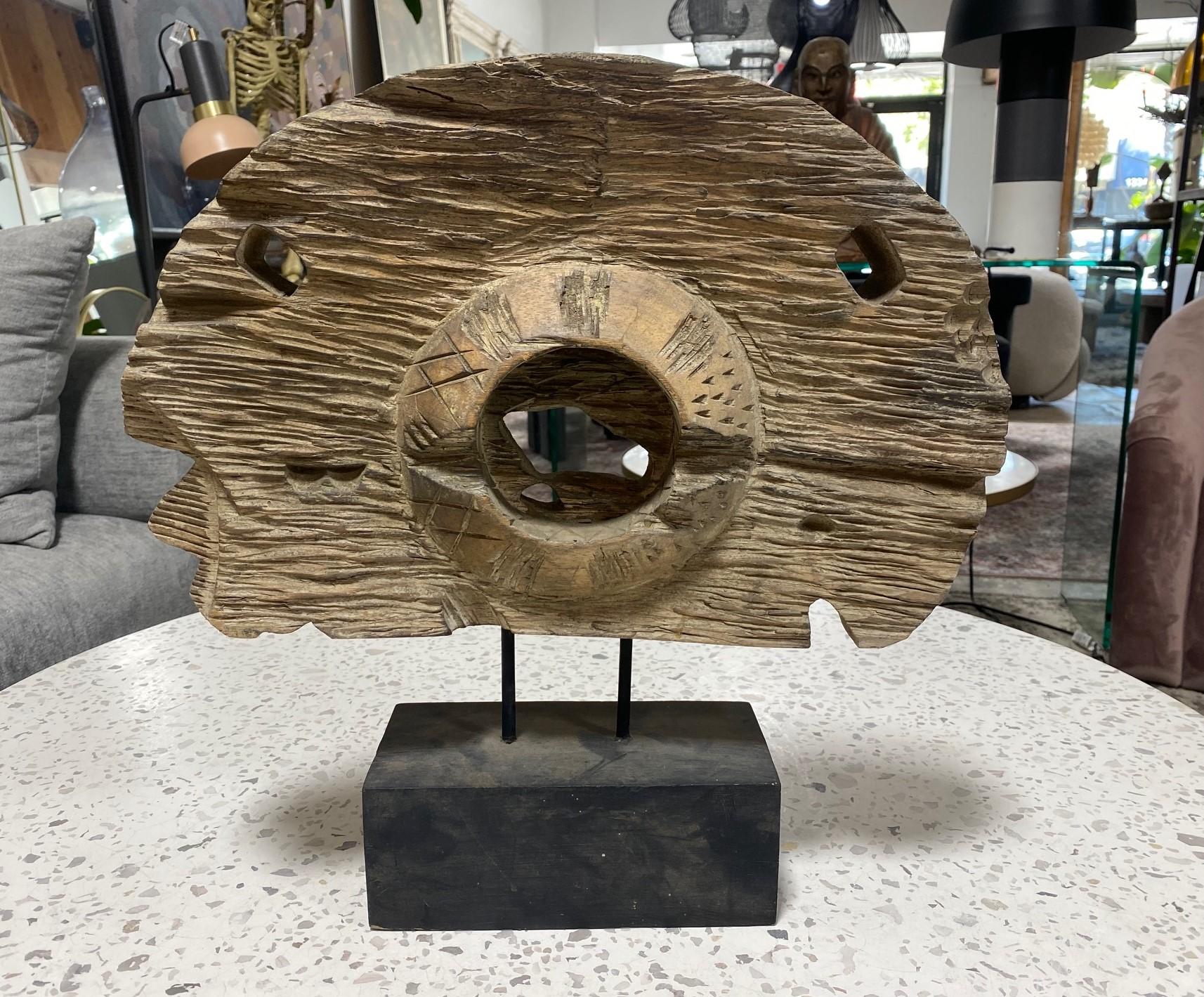 A rather engaging modern abstract folk art wood sculpture on a display stand.  The piece is hand-carved from a single piece of lighter wood (notice the various symbols and indigenous tribal-like markings).  Quite unusual and unique.  

From a Los