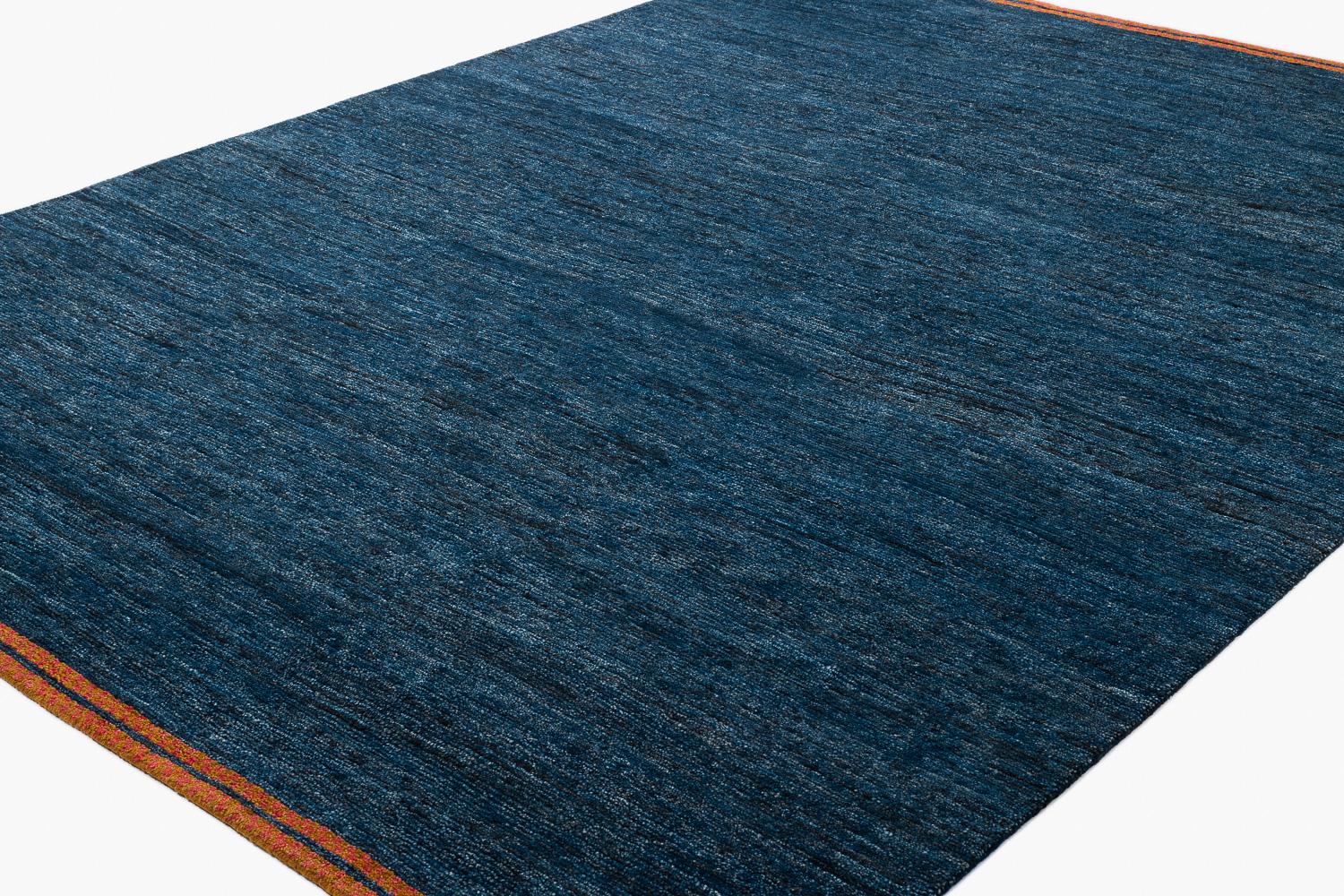 Esta alfombra lisa no tiene nada de aburrida. El rico fondo azul índigo tiene tanta profundidad y variación que sólo puede conseguirse mediante el tinte vegetal natural. Los extremos están ribeteados con un bonito borde en damero rojo y naranja. Con