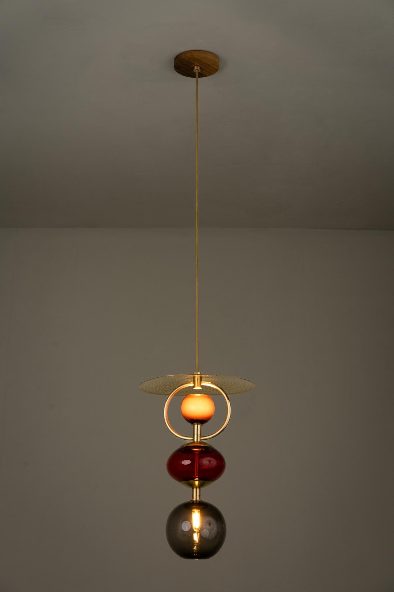 VITRA RED pendant light was designed for the Atomic collection by Mexican artist Isabel Moncada.

The fascination produced by the light through the colors of the glass, the curved silhouette, and the hand-forged brass are the elements that come