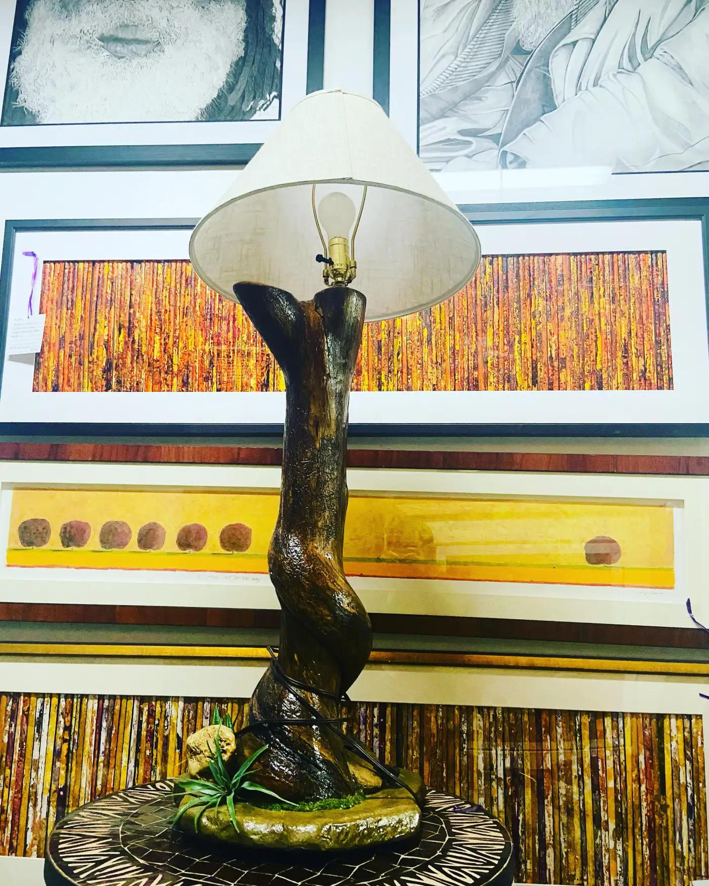 This striking organic modern lamp is a masterful blend of natural elements and contemporary design, embodying the raw beauty of the outdoors while providing functional illumination. The lamp’s base, evocative of a rugged piece of driftwood, is