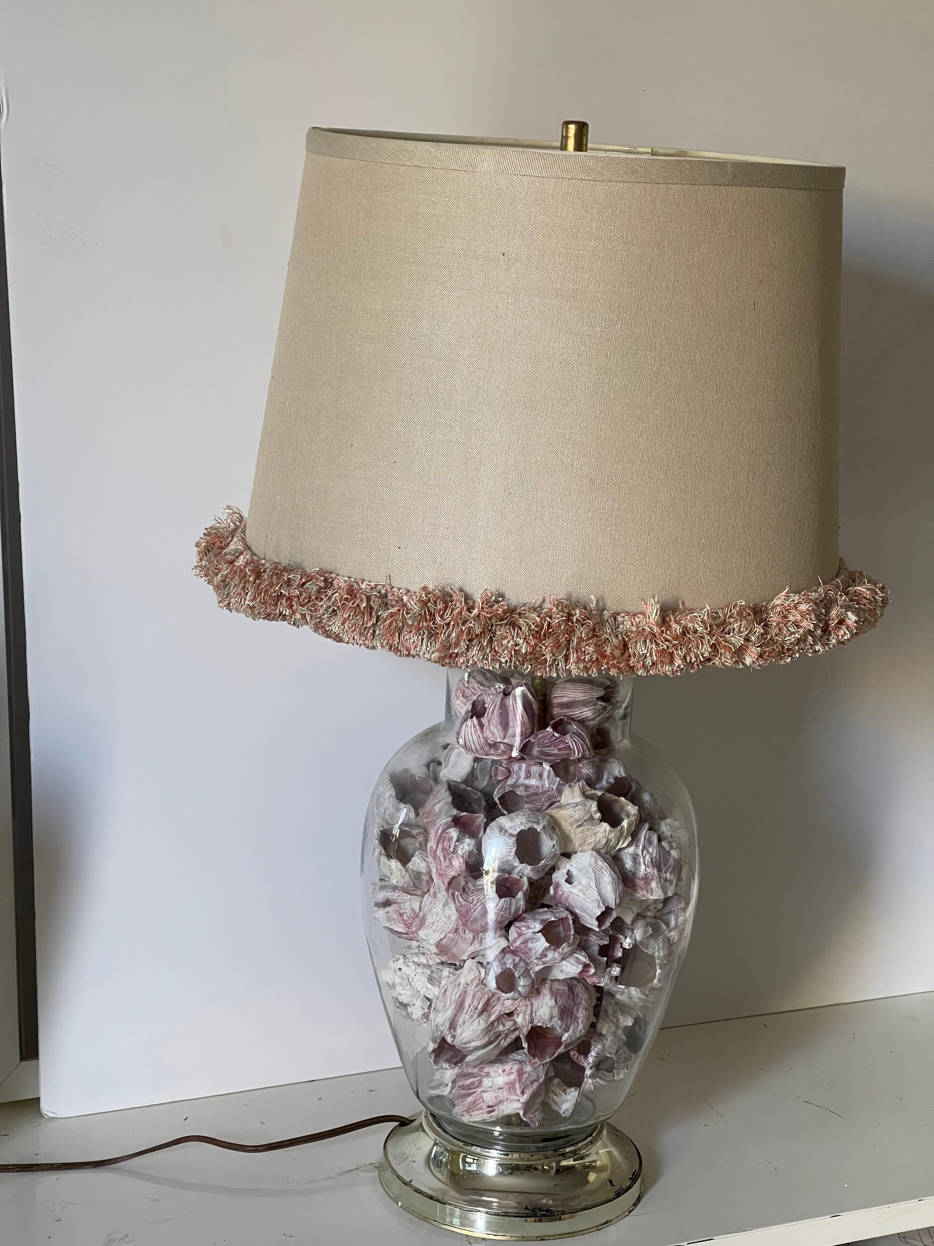 Organic modern sea shell barnacle clusters in a glass ginger jar lamp with linen shade trimmed with fluffy fringes. Paint loss at base.