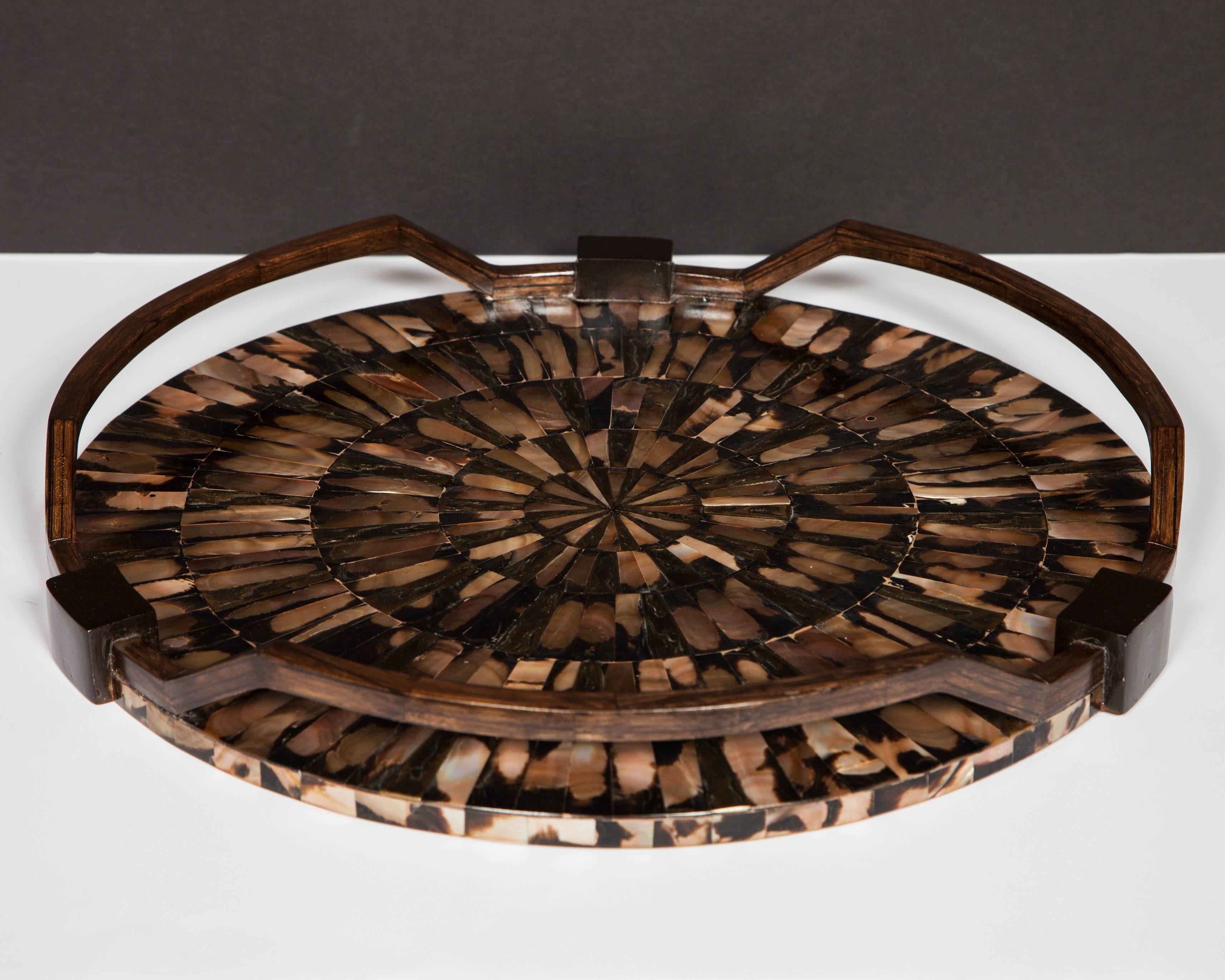 Round serving tray featuring exotic inlays of mother of pearl in varying iridescent hues. The tessellated inlays create a spectacular starburst design. All handcrafted, with a series of hand carved handles in palmwood with ebonized wood block