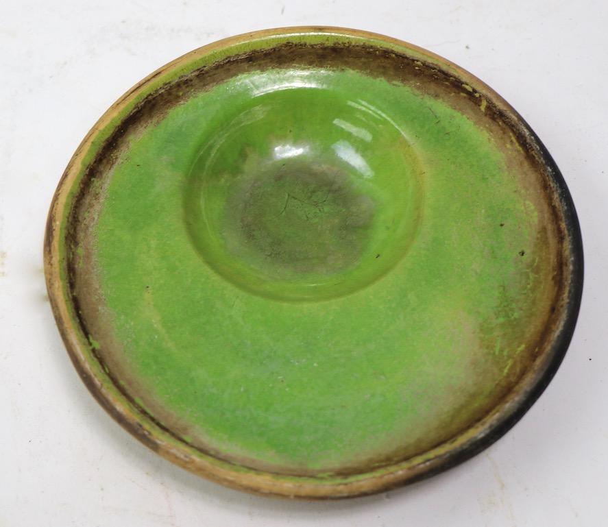 Interesting pottery bowl from the Studio Pottery Movement signed (LAS ? ) dated 1967. Green glaze top with off center indentation bowl, on textured sand colored base. Clean, original condition, free of damage.