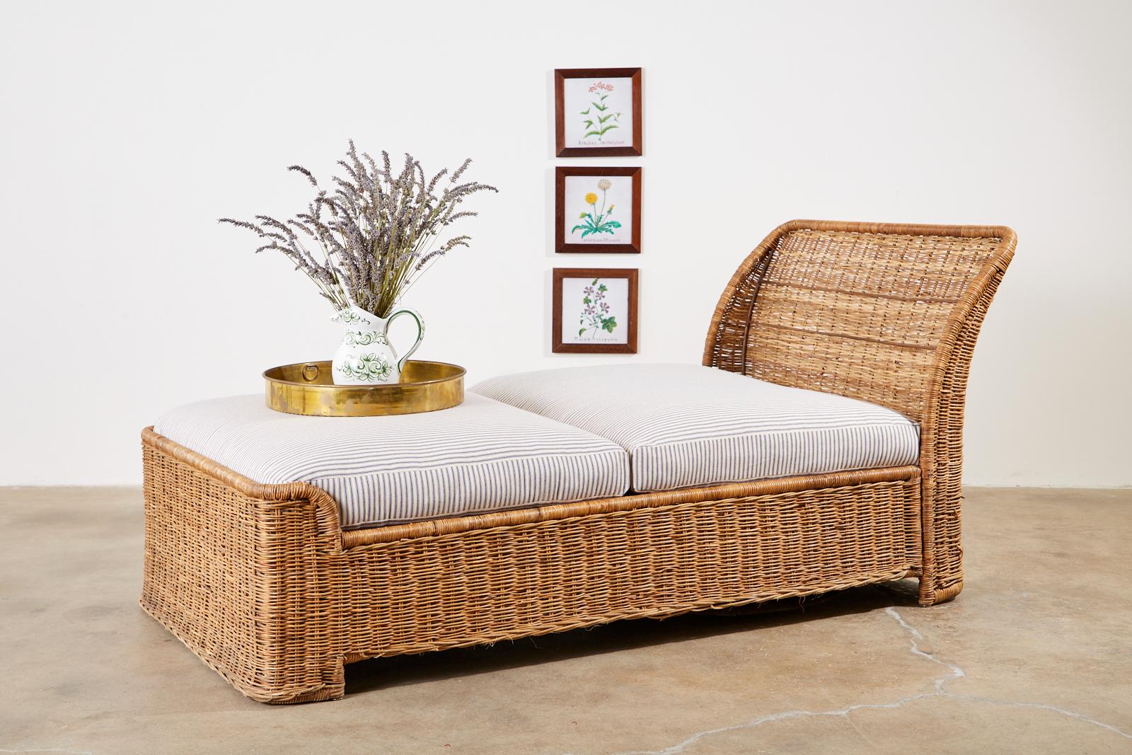 20th century wicker daybed or chaise lounge featuring a sleigh style form. Constructed from a metal frame covered with woven wicker in an organic modern style. Newly upholstered cushions and pillow with classic French blue and white ticking stripe