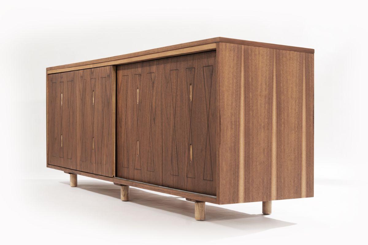 Organic modern credenza or sideboard in the style of George Nakashima, circa 1960-1969. Perfectly executed in walnut, features hand-carved hourglass details on the four sliding doors that open up to reveal adjustable shelving and oak feet.