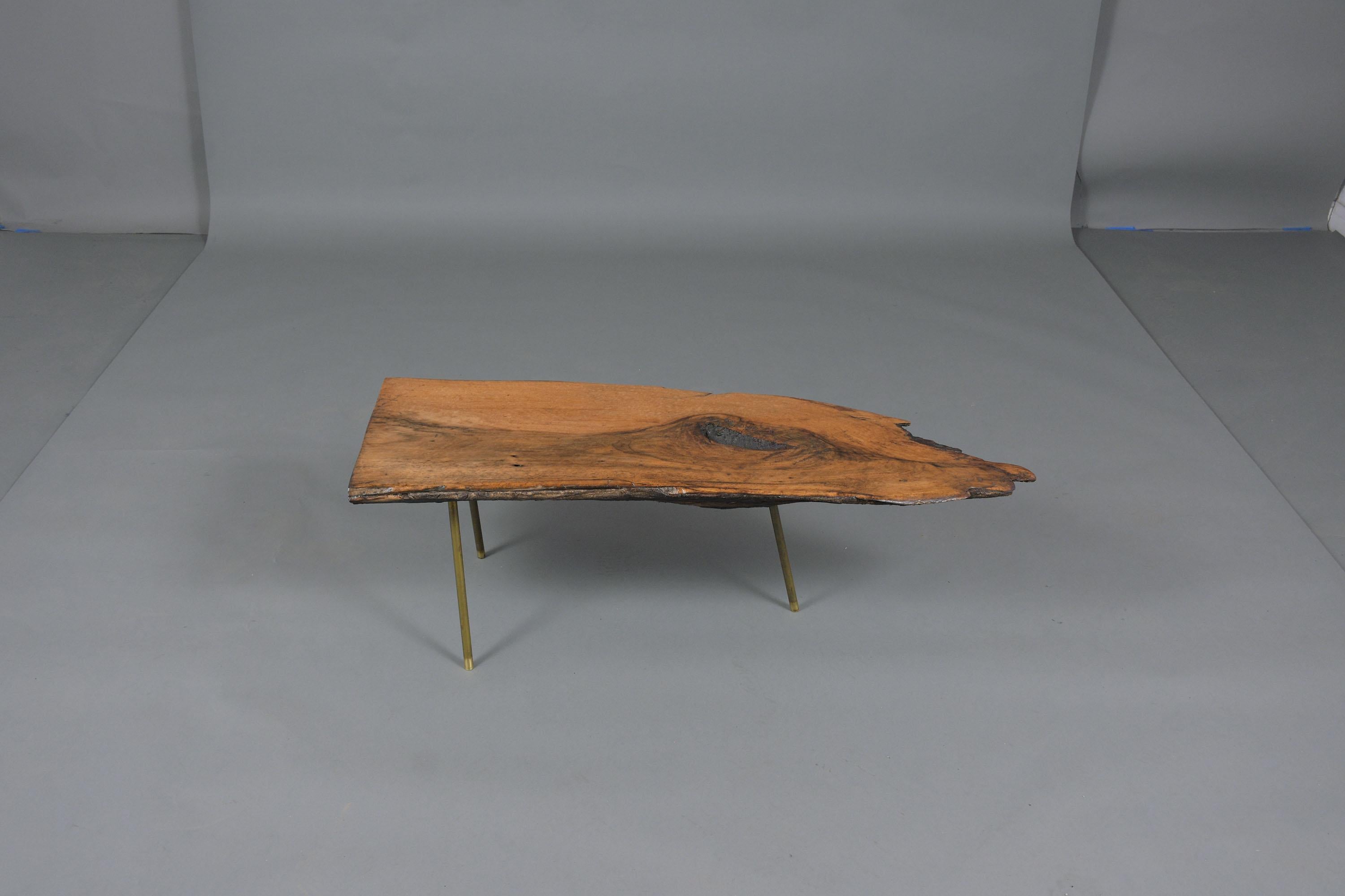 An eye-catching organic modern coffee table in the manner of Carl Auböck crafted out of wood features a free-form wood slab top stained in a natural newly polished with a beautiful patina finish. This intricated side table sits on three solid brass