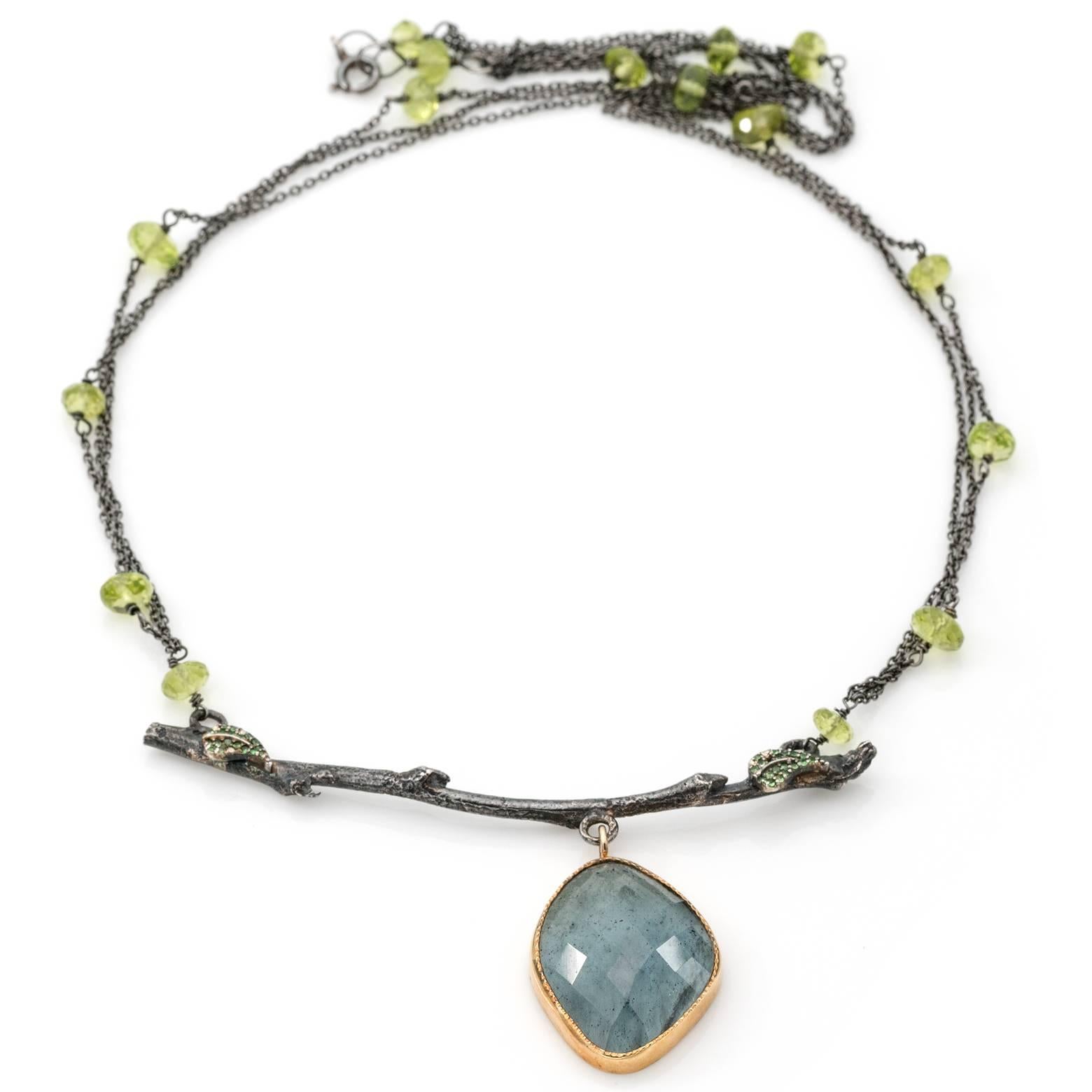 This beautiful organic branch has a a lovey deep blue moss aquamarine pendant with a 14k bezel. The leaves on the branch are tsavorite inlayed balanced on each end and the multistrand chain is intermixed with peridot beads to complete this gorgeous