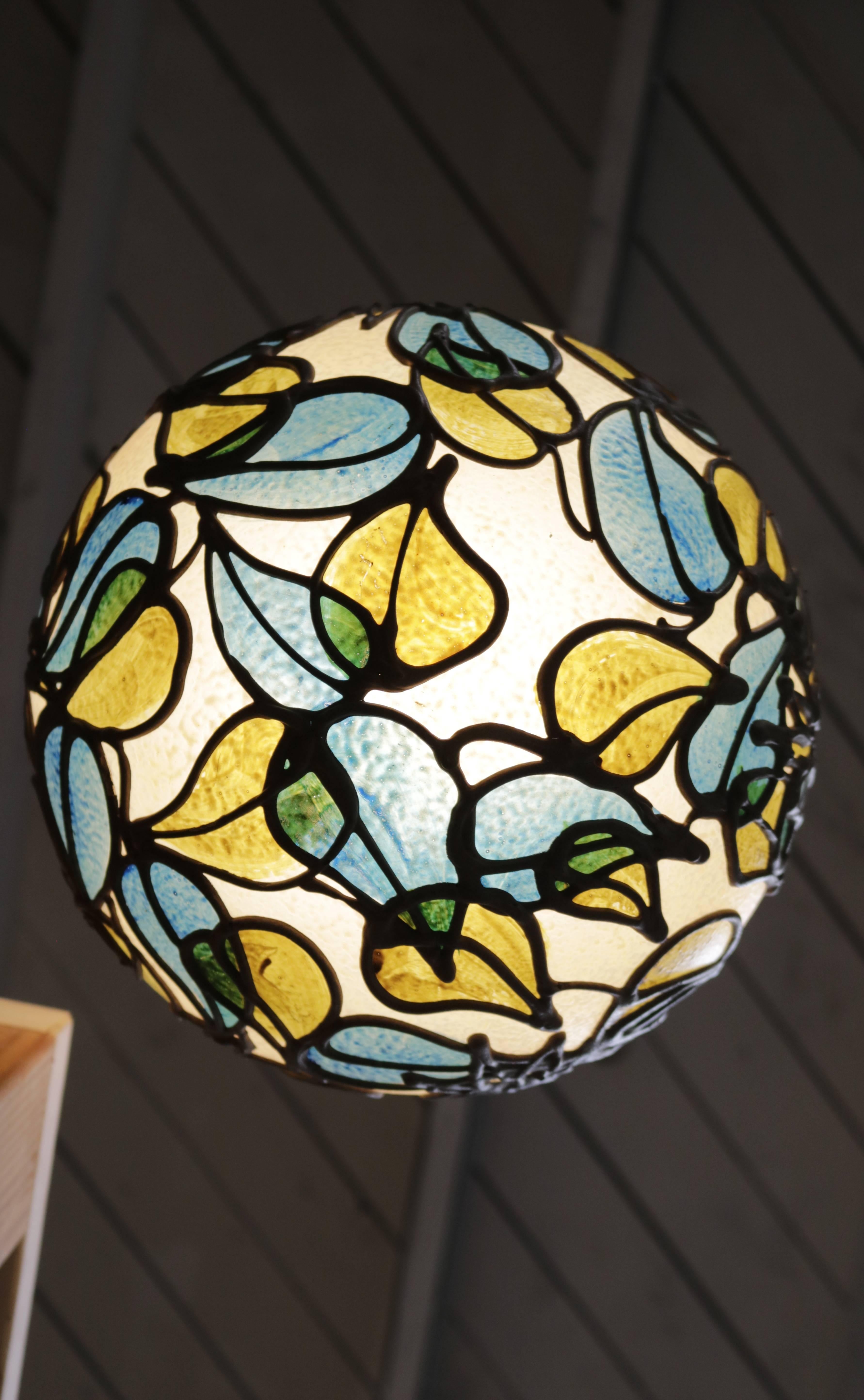 Hand decorated resin globe hanging from a hammered brass top. Displays a warm glow when lit.