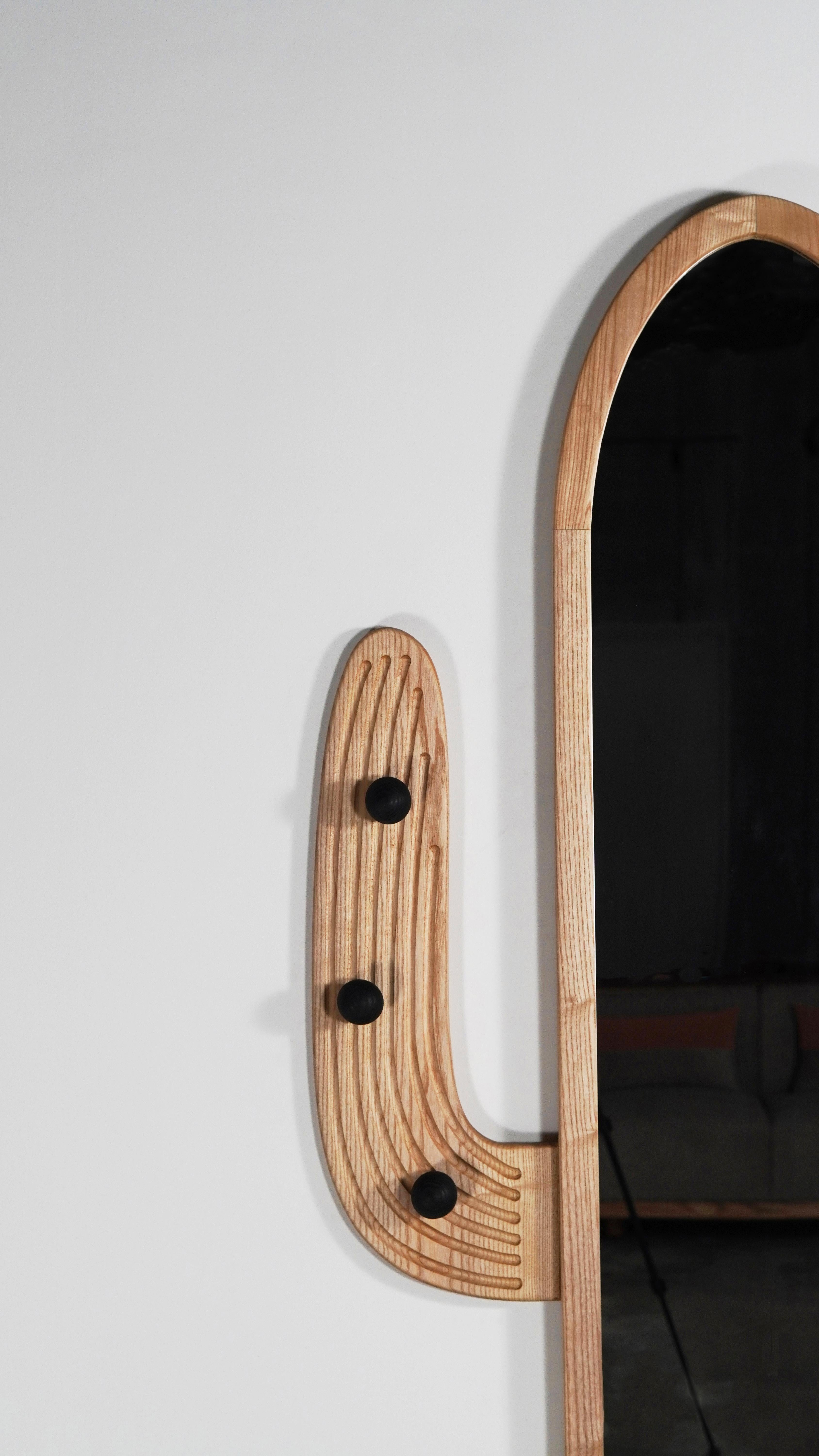 This unique and artistic cactus-shaped wall mirror, handcrafted in solid American Ash wood, adds a touch of the desert to your space. This wall mirror goes beyond reflection, boasting fine grooves and wooden details that provide a tactile and