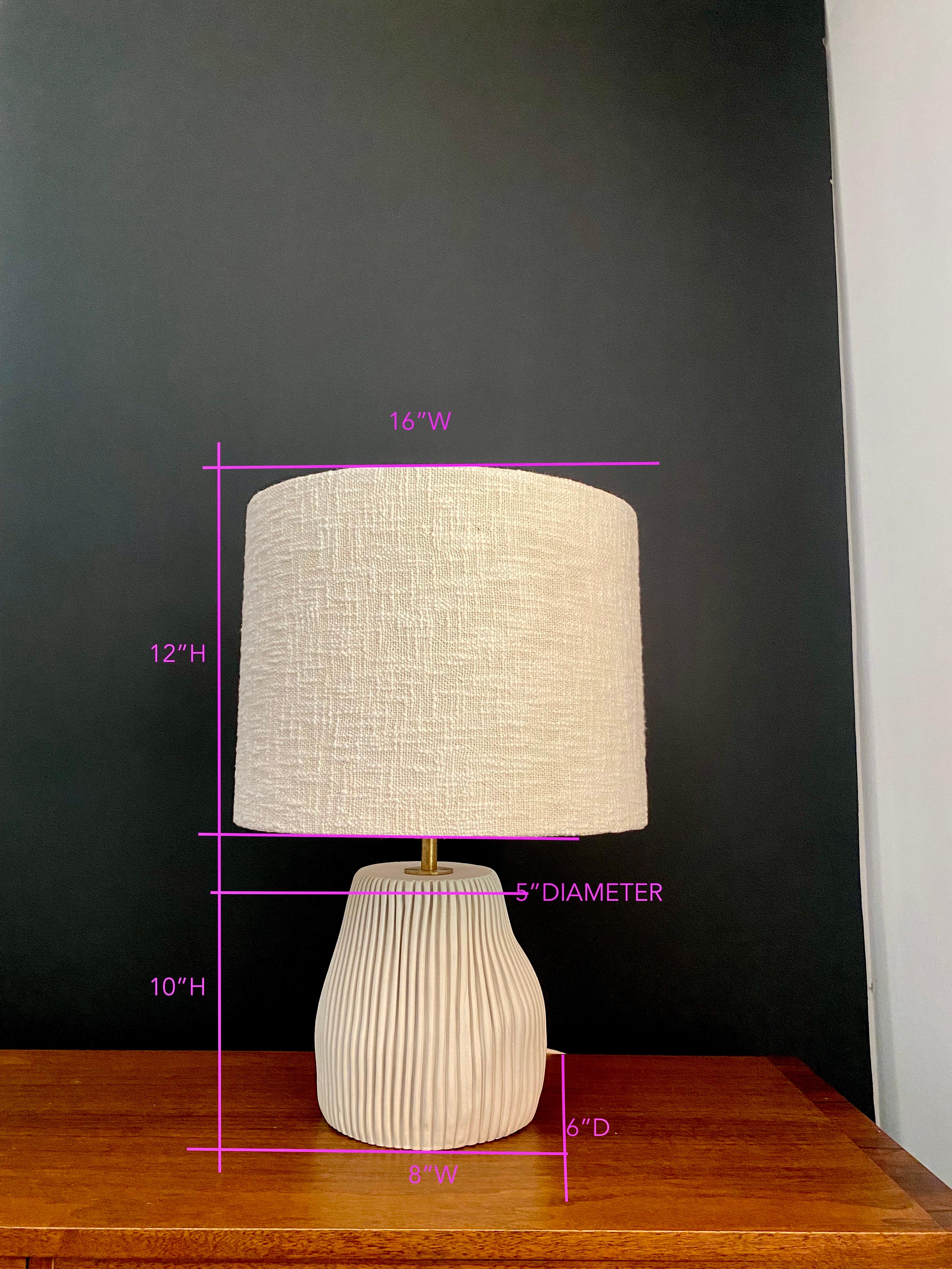 Porcelain base,
6’ cloth covered cord. 
Solid Brass adjustable harp, 
Brass hardware w/ LED dimmer on socket. 
Linen, Burlap or handwoven Bouclé custom lamp shade.
Base Dimensions: 11”High x 10” Wide x 7” Deep (+/- 1