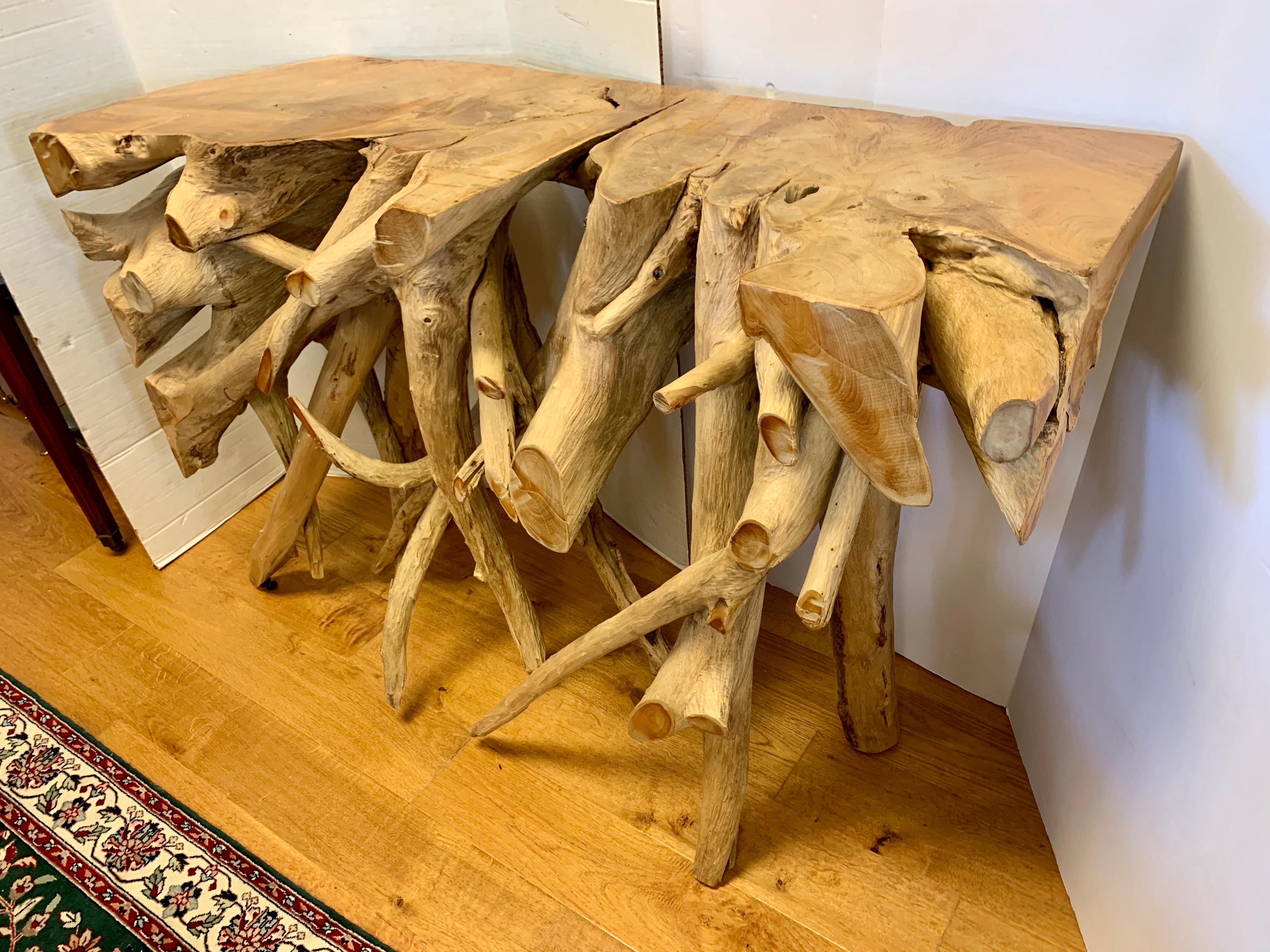 A unique teak tree root console table measuring four feet wide. This wooden console table has been custom fashioned from a large cut section of old teak whose intertwining roots give it an organic and airy feel. 

There is a unique contrast of