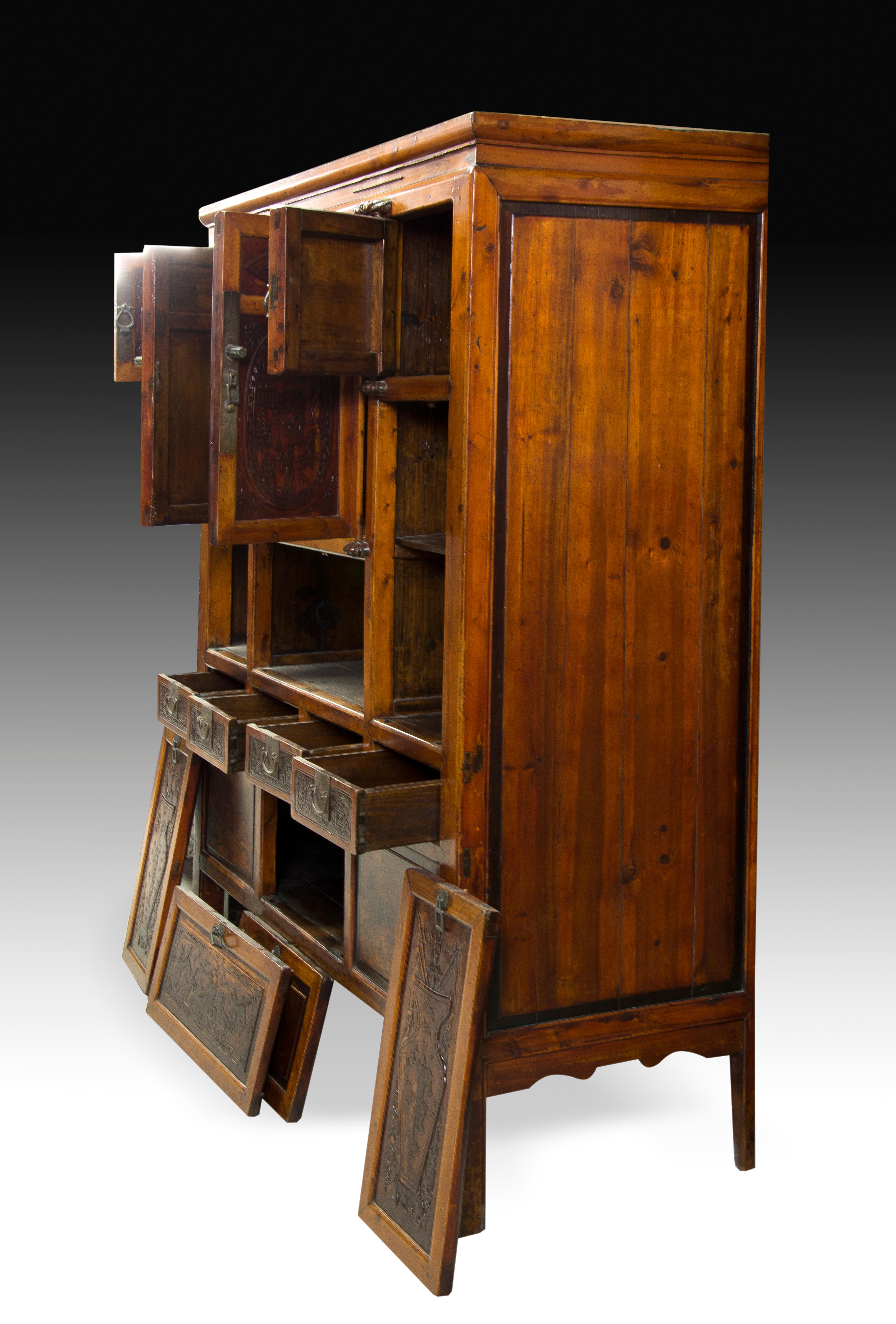 High cabinet made of carved wood, with metal fittings, which has a decoration with a certain oriental influence. In the upper part it has two doors in the center and two smaller ones on the sides, these located on two covered spaces that give access