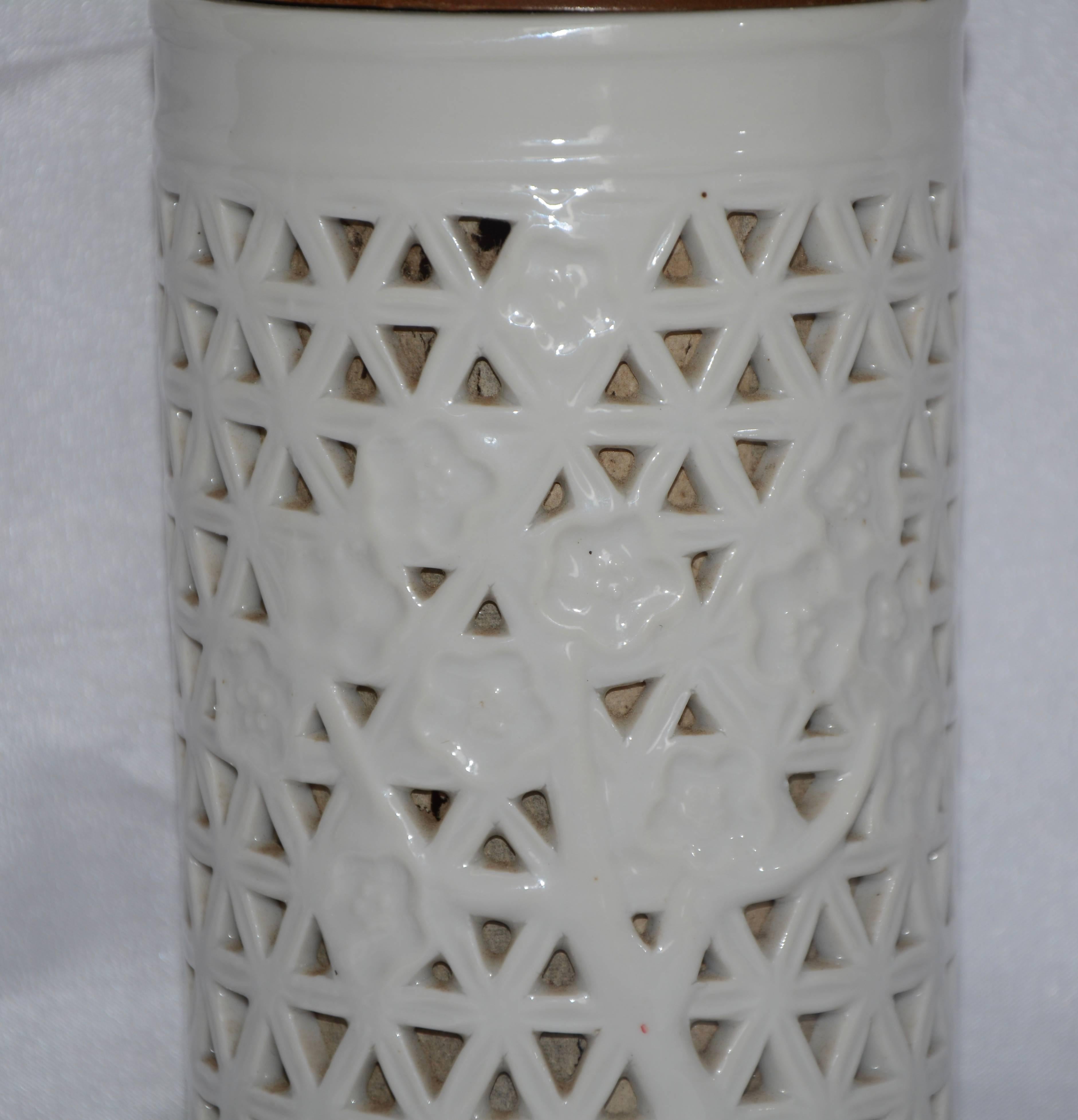 Cherry blossoms accent this Blanc-de-chine off-white ceramic lamp. The pierced porcelain is lined with paper and the top and bottom are made of wood. The push-thru socket turns on the top socket and also a soft light enclosed inside the porcelain.
