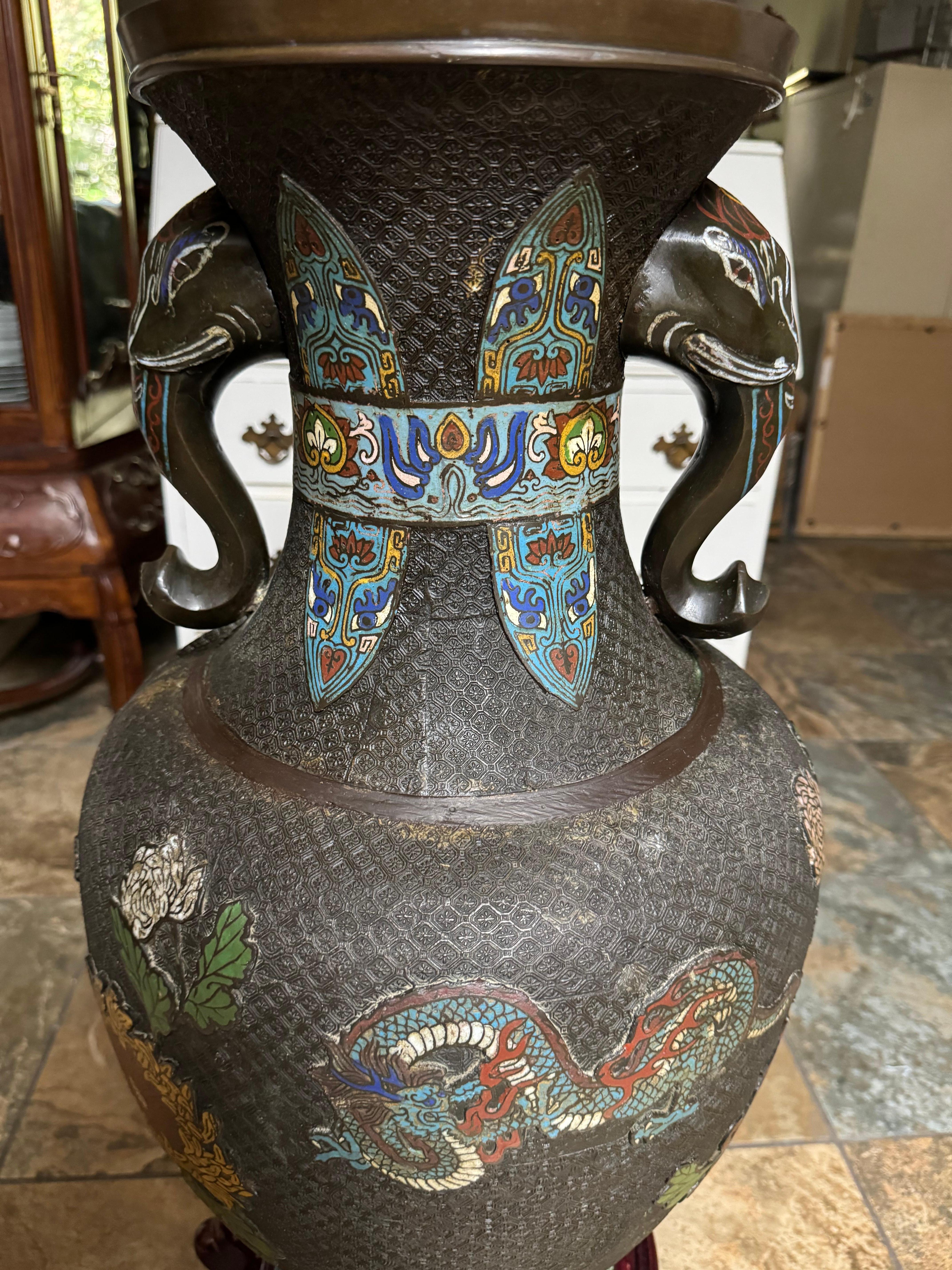 Vaso orientale Champleve Cloisonne Dragons in bronzo con manici a forma di testa di elefante su base di legno.  Potrebbe essere della fine del XIX o dell'inizio del XX secolo, in base alle mie ricerche su Google di oggetti simili.  

Presenta un
