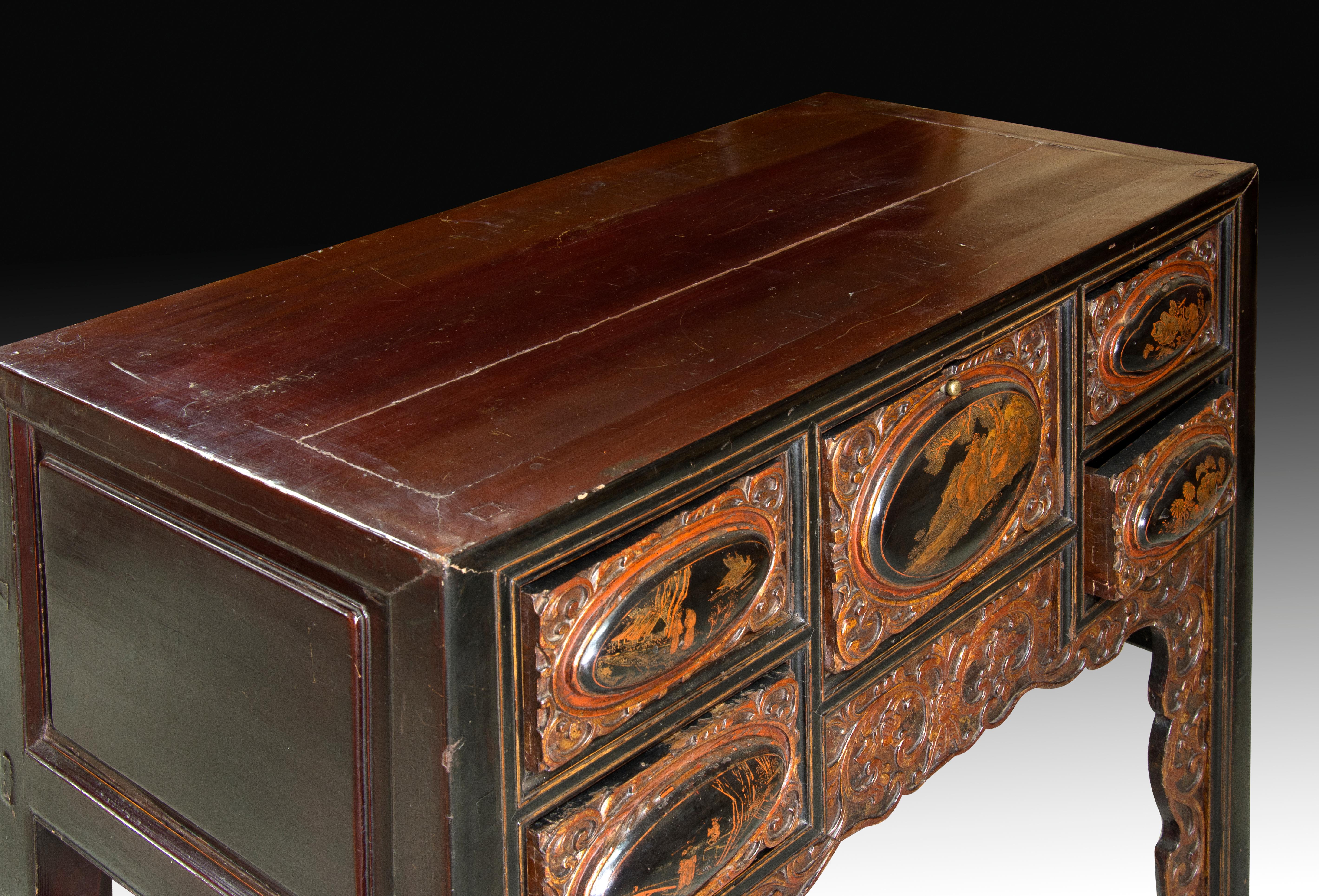 Rectangular and straight upper board furniture decorated on the sides with geometric elements and in front with an elaborate carved plant elements enhancing the ovals present in its five drawers, in which floral compositions and figurative scenes on