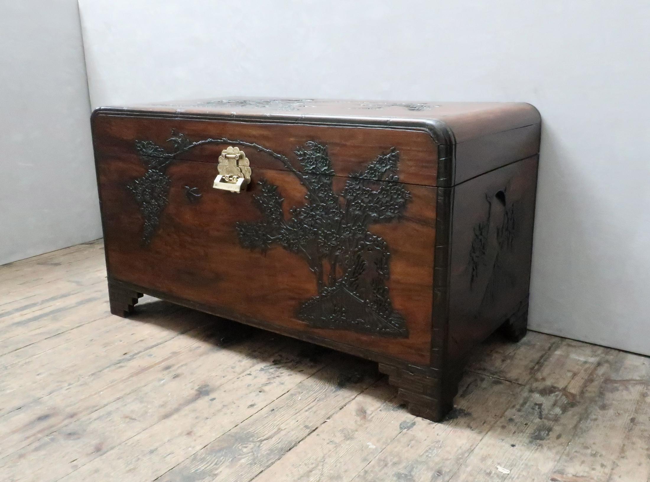 A very good quality early 20th century oriental freestanding camphor wood chest with relief carving of cherry blossom trees, birds and flowers to all four sides and top with simulated bamboo carved edges stood on simulated bamboo carved bracket
