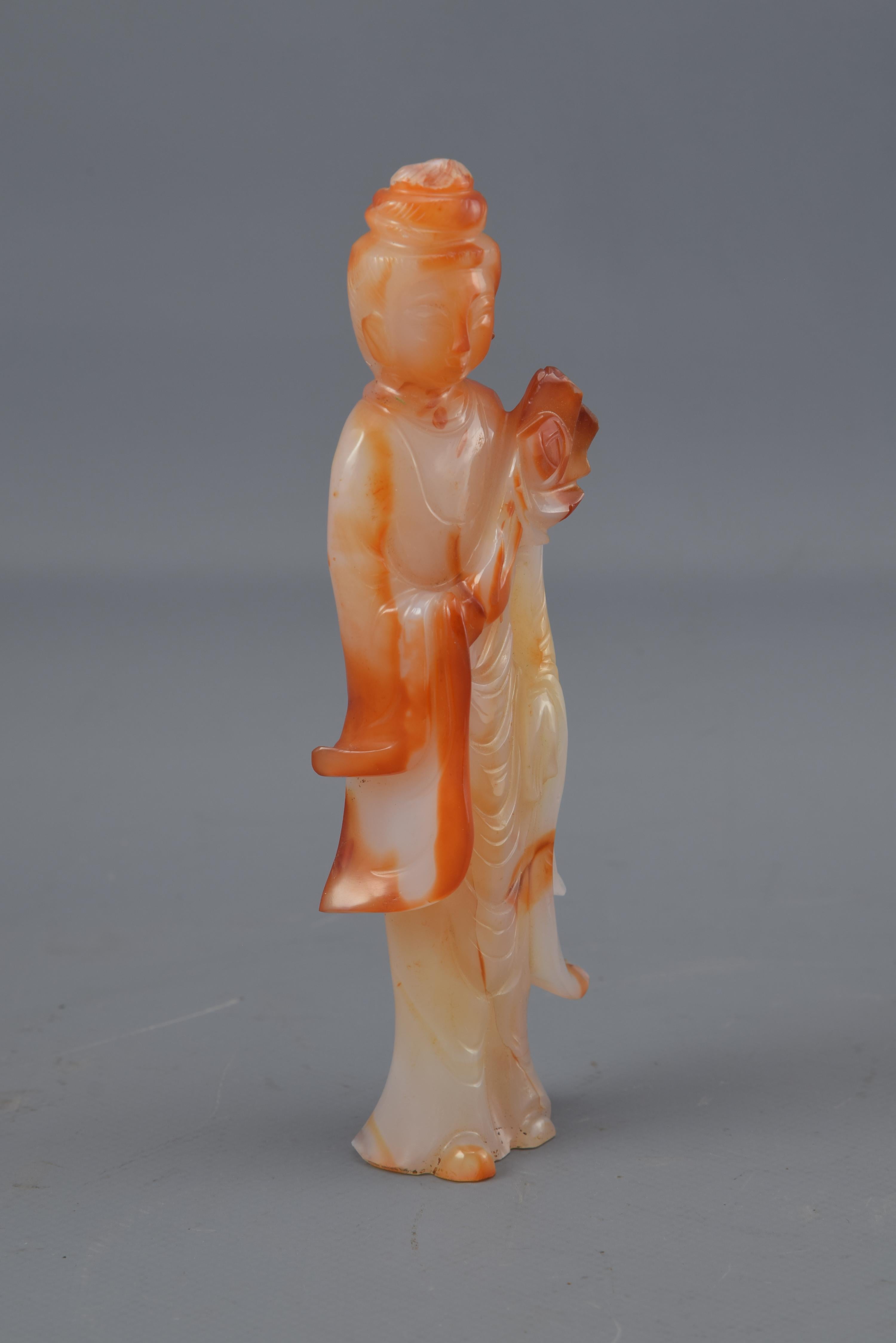 Figure stylisée en pierre dure de couleurs blanche et orange, avec des variations tonales frappantes, qui représente peut-être l'un des huit immortels du panthéon taoïste, He Xiangu (qui est généralement représenté tenant une fleur de lotus, parfois