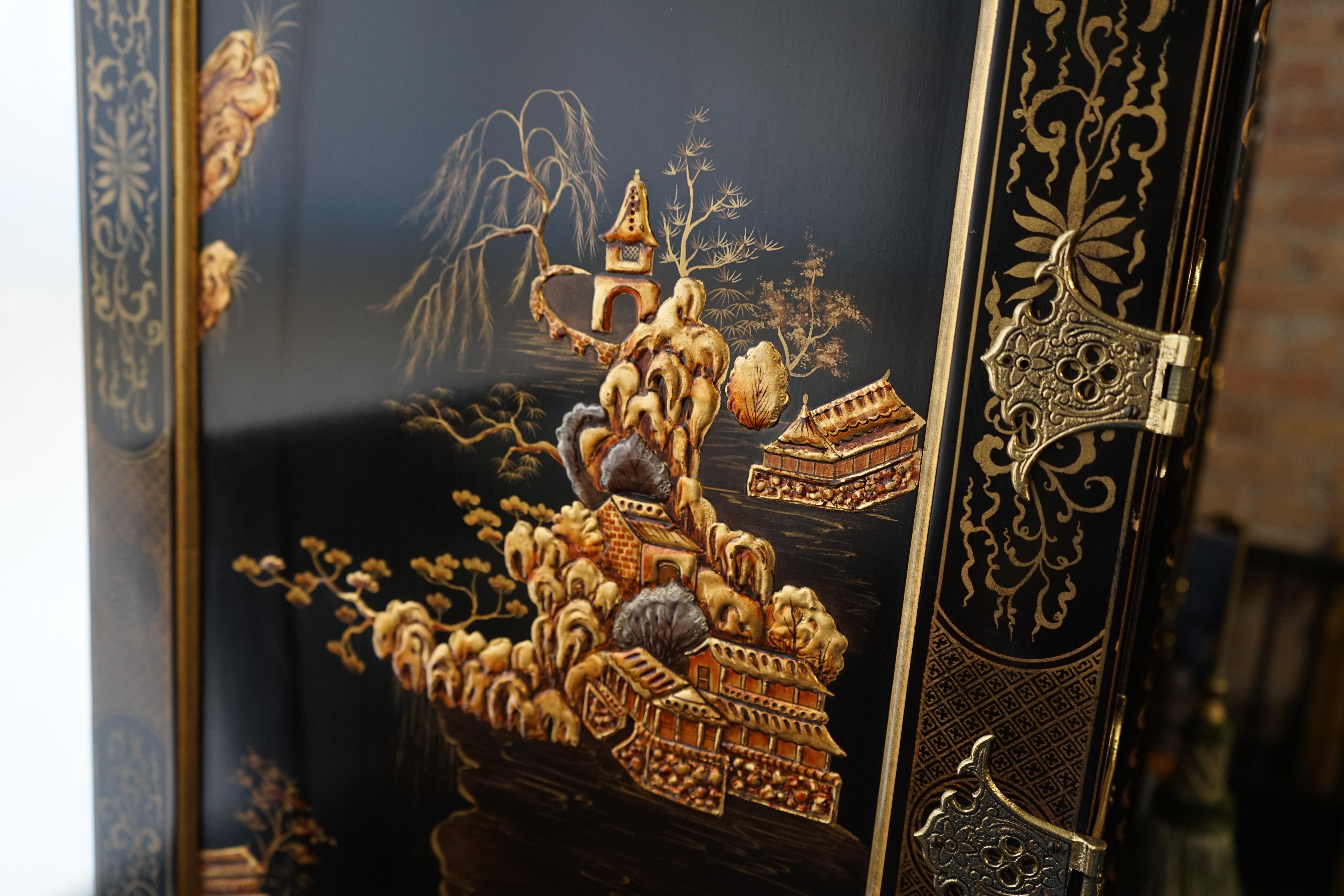 Simply stunning, ornate, black lacquer cabinet from The Stately Homes Collection by Baker Furniture. It features a stunning case that was  elaborately decorated (painted) in a raised gilt and ochre landscape design.  It is rumored that the case was