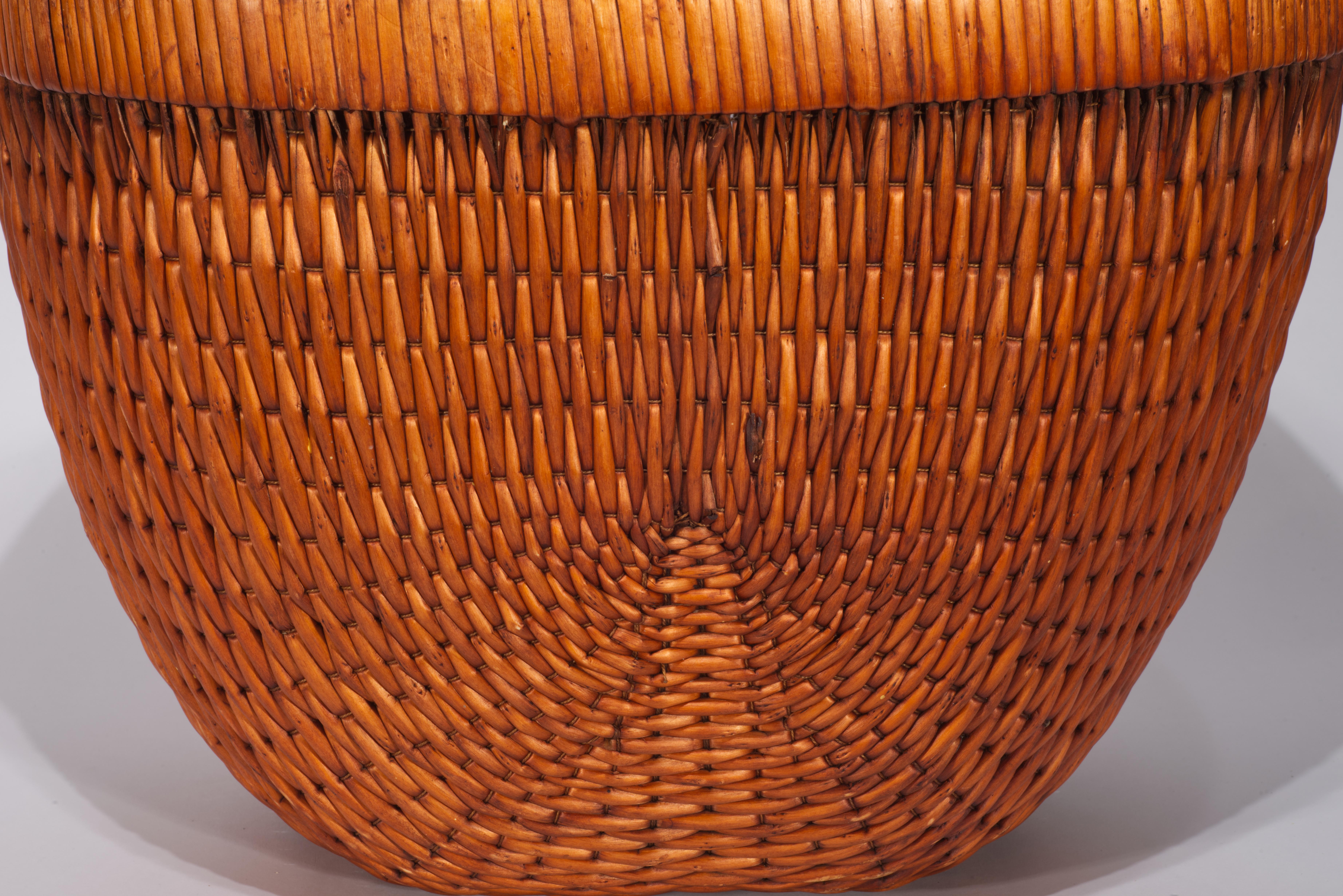 Vintage Chinese style fisherman or grain basket features the traditional shape with rounded sides and flat wooden rim wrapped with wicker. The strong, flexible wicker or willow strips are skillfully woven into a delicate pattern that emphasizes the