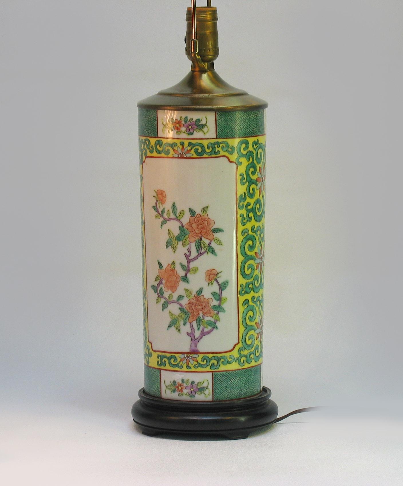 Une porcelaine orientale
Famille verte cylindrique
Vase monté en lampe
20ème siècle.

Décoré de cartouches sur les deux côtés, 
avec des branches fleuries, le tout sur un fond jaune 
avec des gerbes vertes défilantes, 
sur un support en bois