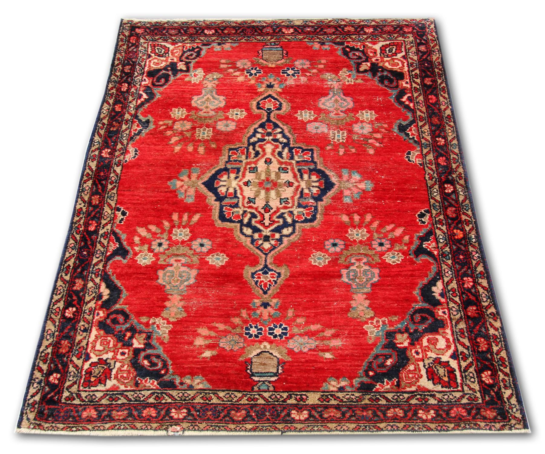 This fine wool rug is a handwoven masterpiece, constructed by hand this piece features a rich red background with a large central medallion and symmetrical vase surrounding design. This has then been framed by a repeating pattern border. Both the