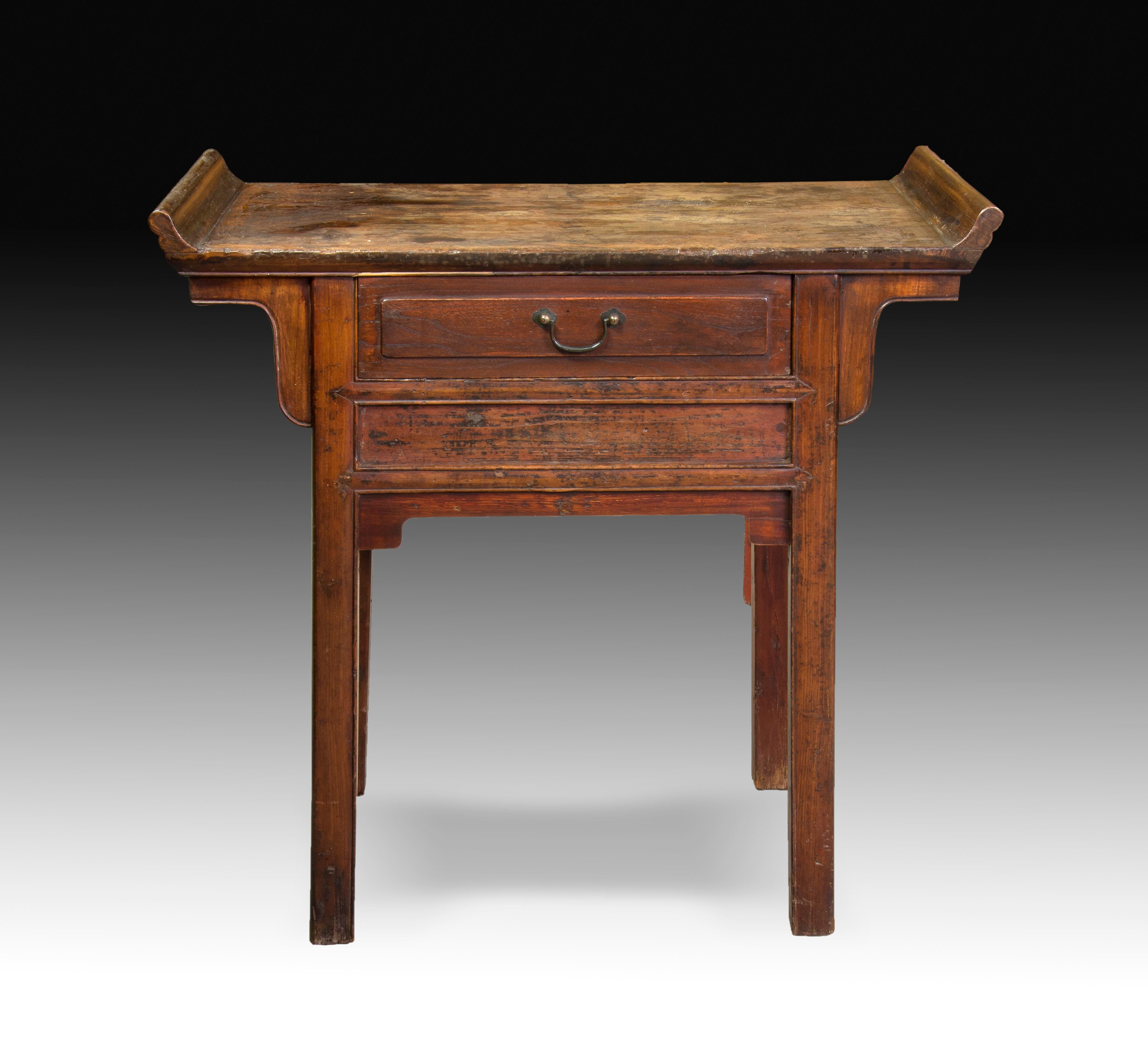Oriental table. Carved wood, metal. Twentieth century. 
Side table made of carved wood, with a rectangular top board decorated with two highlights on its smaller sides and a drawer in front. Both its shape and its decoration (simple, present on the
