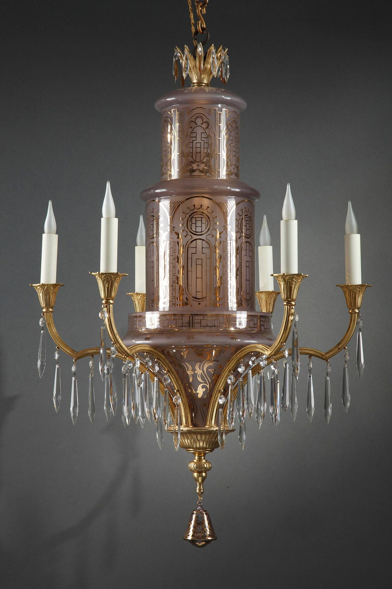 Elegante lampadario in stile orientale in cristallo colorato rosa e bronzo dorato con sei bracci luminosi, composto da un fusto illuminante formato da due cilindri sovrapposti, tutti decorati con fili d'oro geometrici e fogliati. I bracci luminosi,