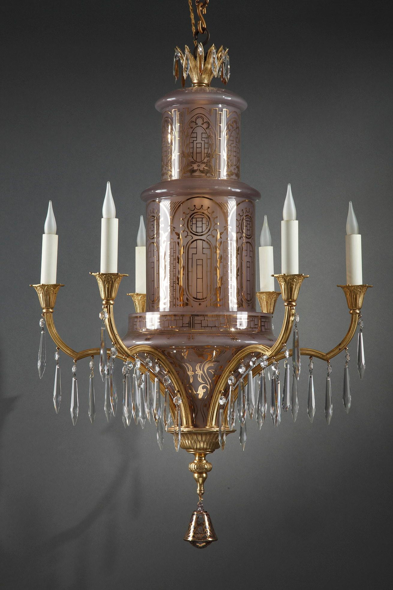 Elégant lustre de style oriental en cristal teinté rose et bronze doré à six bras de lumière, composé d'un arbre d'éclairage formé de deux cylindres superposés, tous décorés de fils d'or géométriques et feuillus. Les bras de lumière, qui suivent la