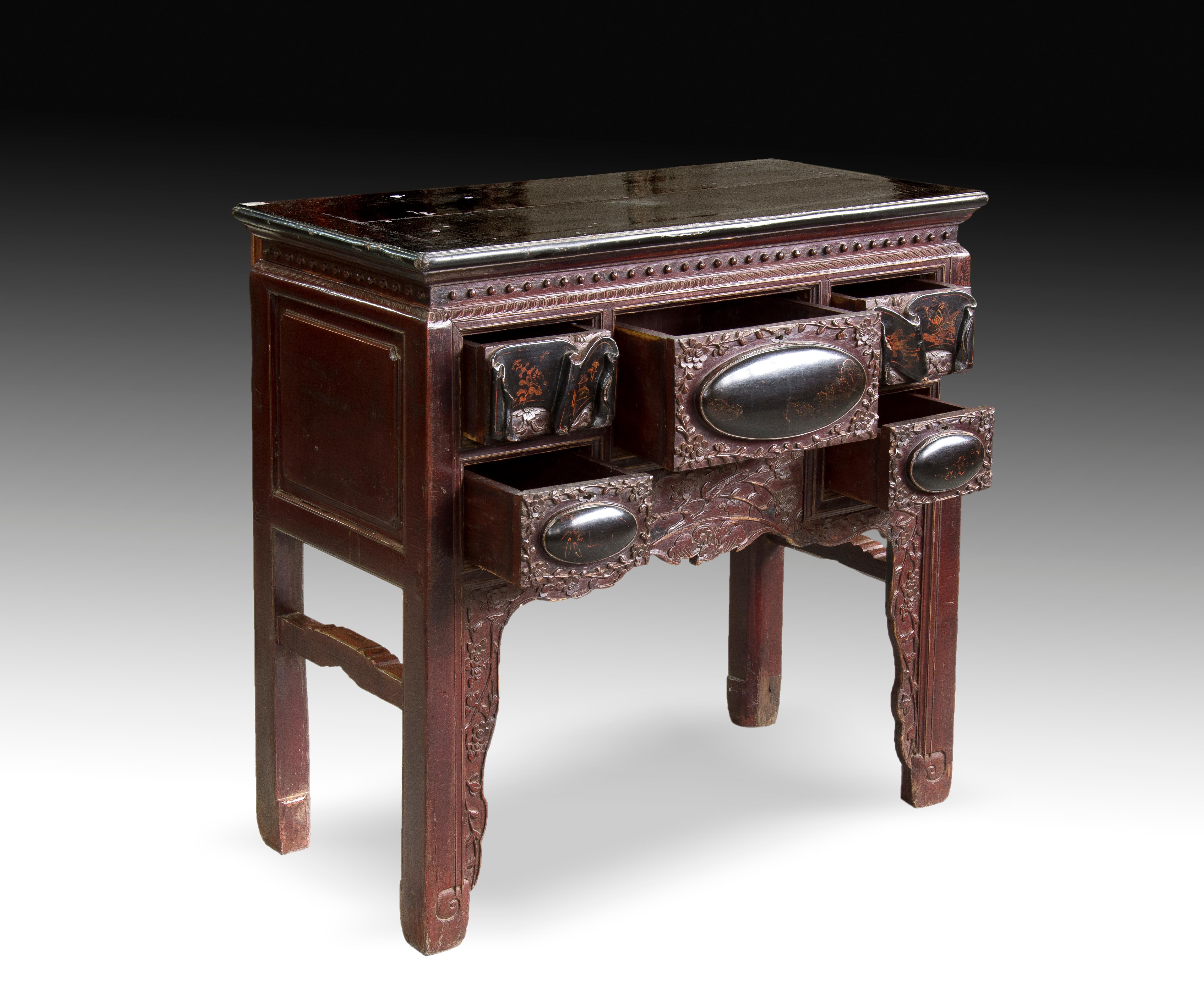 Four-legged table with a rectangular board slightly protruding from the body of the piece of furniture and a front carved in relief not too pronounced, clearly distinguishing each of the five drawers it presents. Both the decorative motifs, the