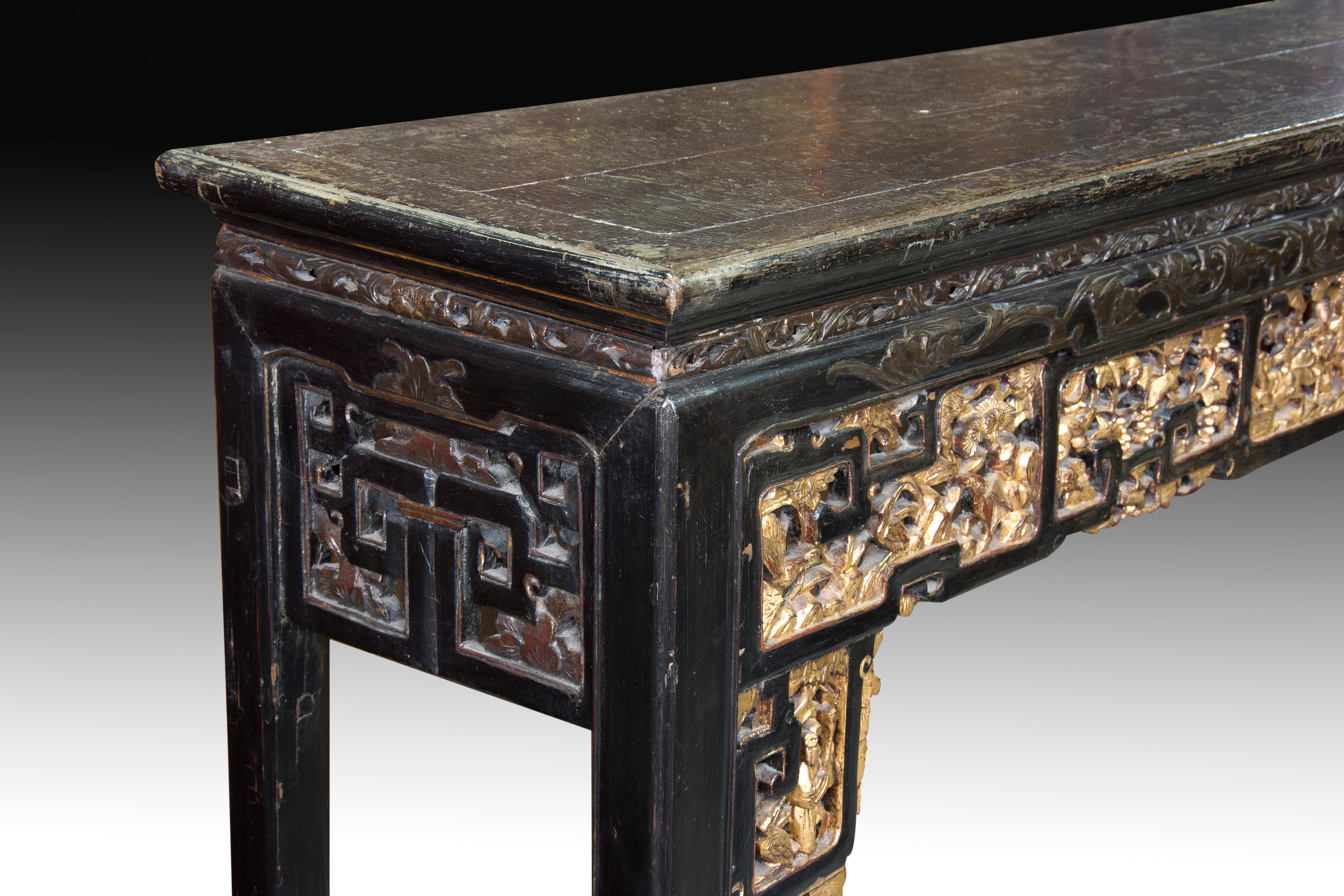 Rectangular table of smooth board with four square legs decorated with fine carvings organized in geometric shapes. In front, these have been gilded to enhance them. Both these figurative compositions and the lines and proportions of the furniture