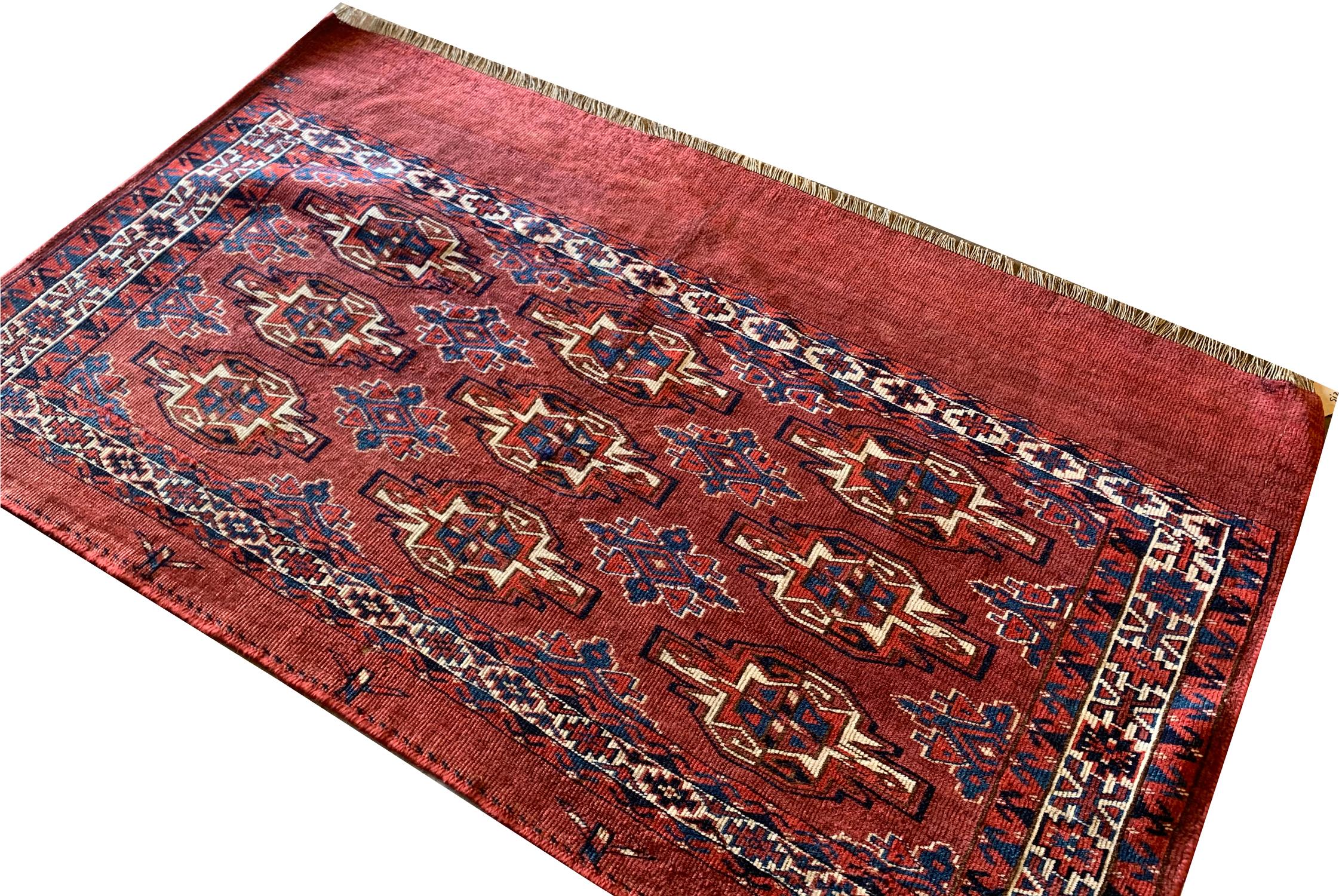 A geometric tribal design has been woven on a rich red background in blue, beige and brown accents by Turkmen tribes; This piece is an antique Chuval style rug, woven in the 1880s with sophistication and traditional motifs and patterns. The bold