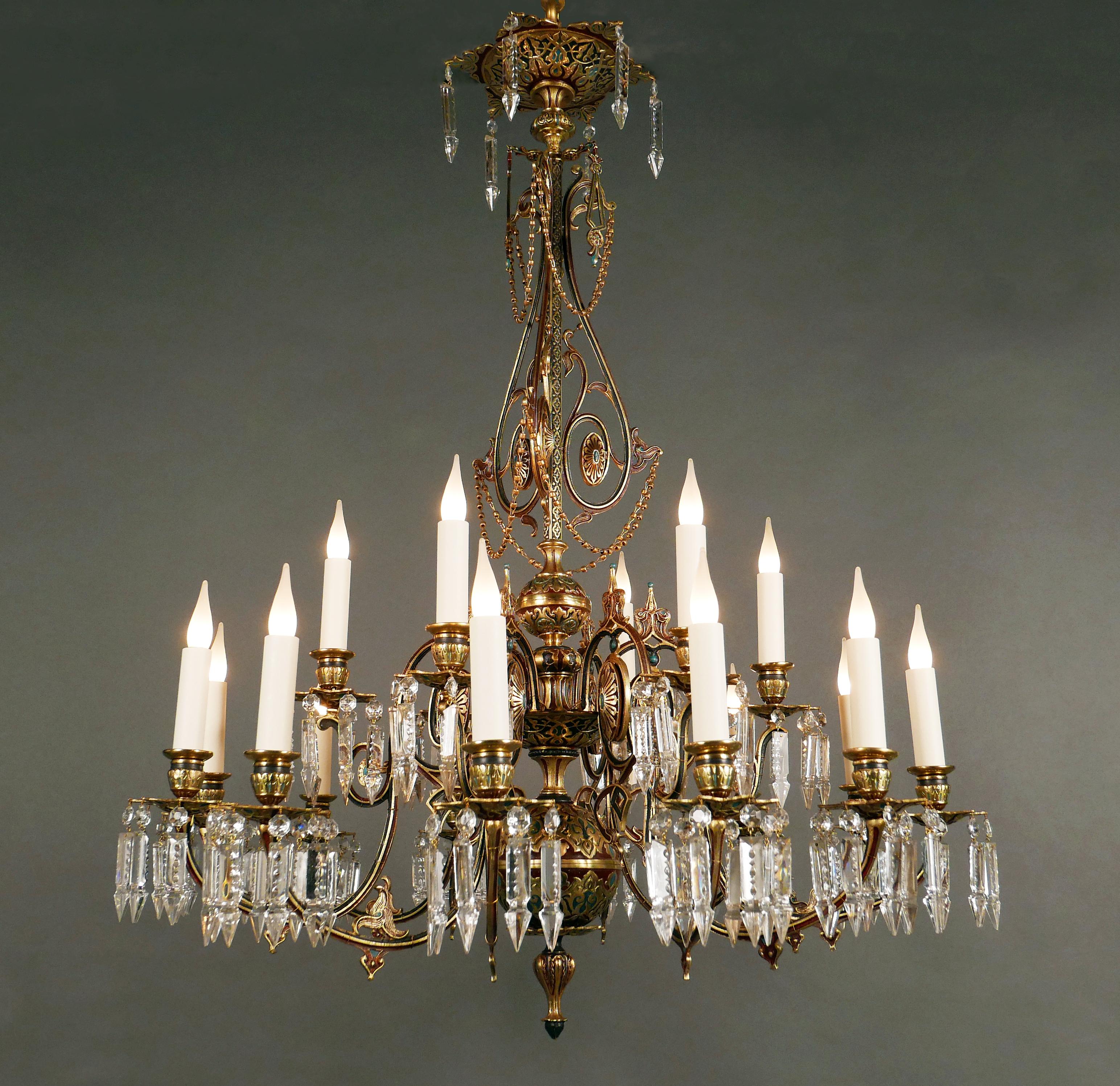 Rare chandelier in gilded and patinated bronze with eighteen lights, finely decorated with stylized oriental motifs in polychrome red and blue cold enamel. Surmounted by an elegant ceiling light, it consists of a shaft embellished with interlacing