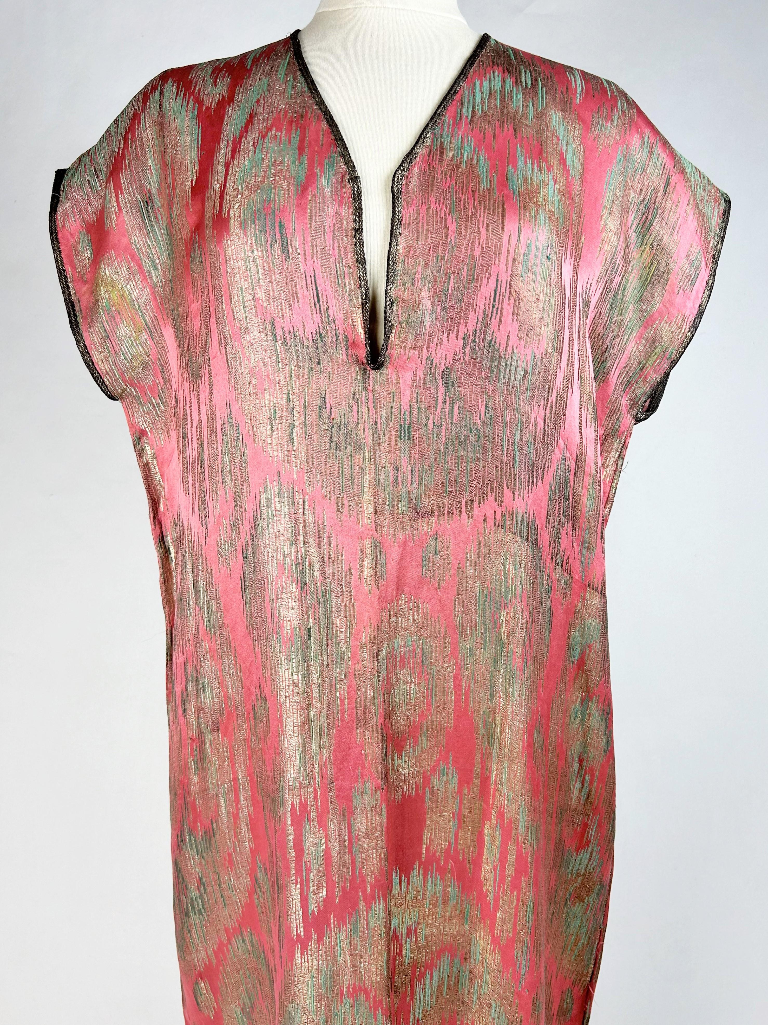 CIRCA 1915-1920
Frankreich Paris
Orientalisches Kleid oder Djellaba aus Lamé, inspiriert durch das Ikat-Muster der Adras-Seiden aus Buchara in Usbekistan. Minimalistischer Sackschnitt, ärmellos, weit und gerade, mit silbernen Lamé-Paspeln an den