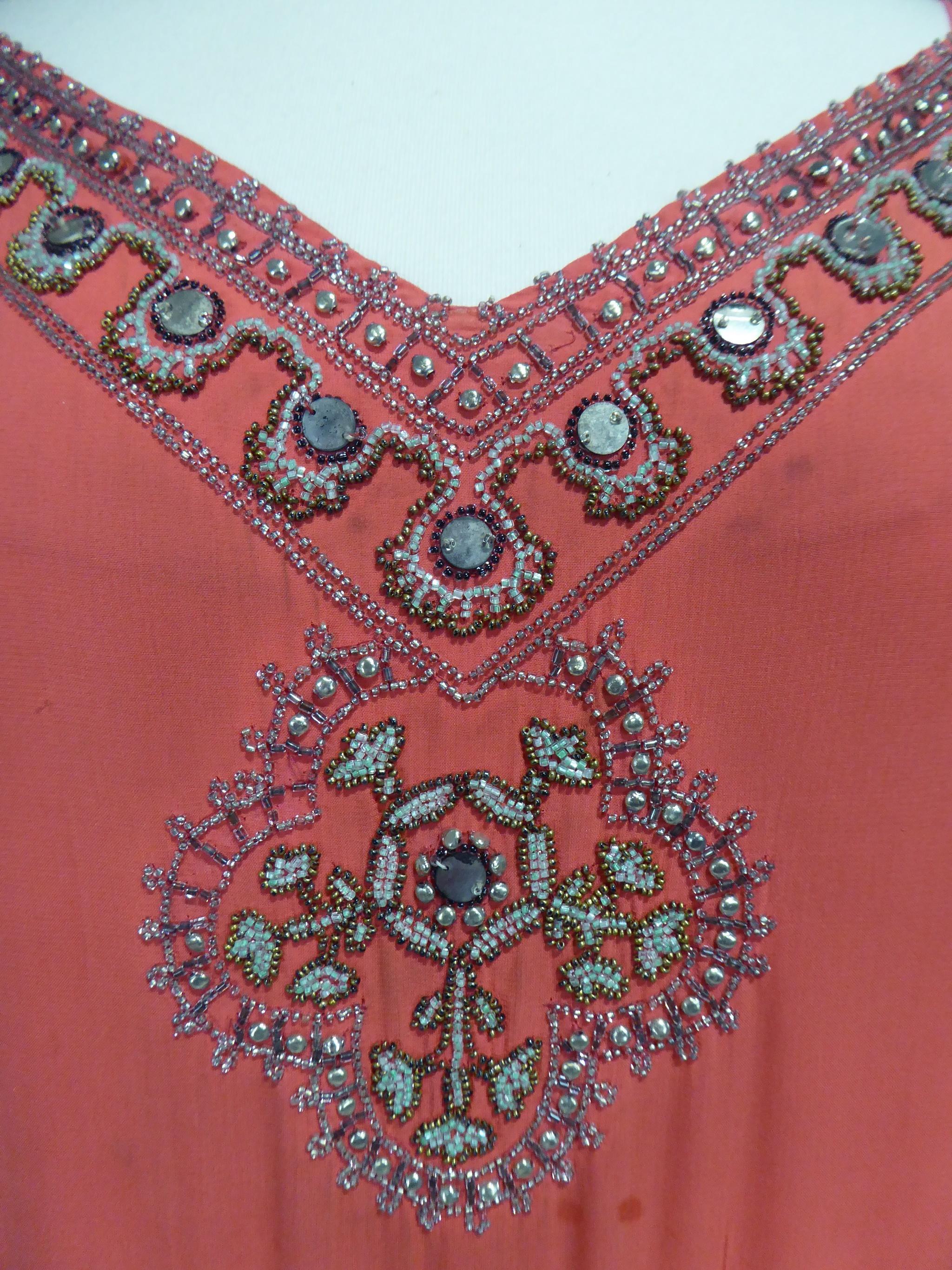 Um 1925
Frankreich

Ballkleid oder Flapper-Kleid aus korallfarbenem Seiden-Crêpe:: bestickt mit Perlen und Spiegeln aus den Roaring Twenties. Zwei lange ärmellose Bahnen mit passendem Unterkleid sind an den Seiten des stark ausgeschnittenen Kleides