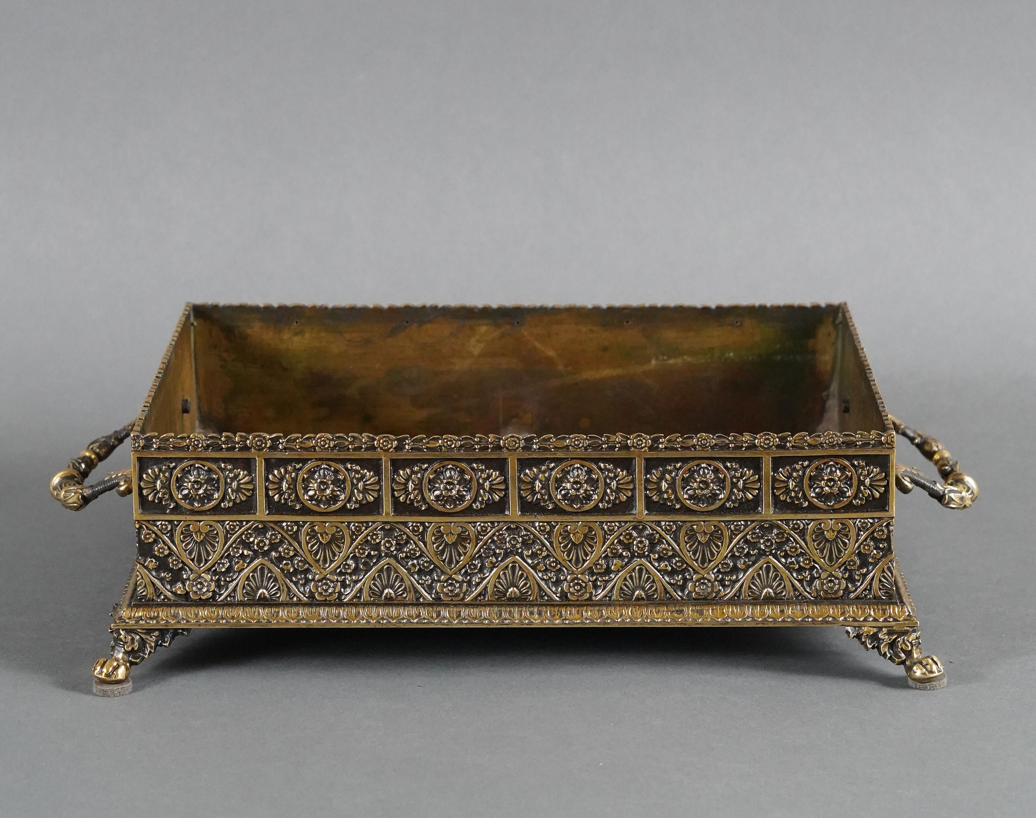 Elegant Orientalist style rectangular planter in patinated and gilded bronze, resting on four lion paws. It is adorned with decorative friezes of water leaves, stylized floral medallions and palmettes on a scattering of flowers.