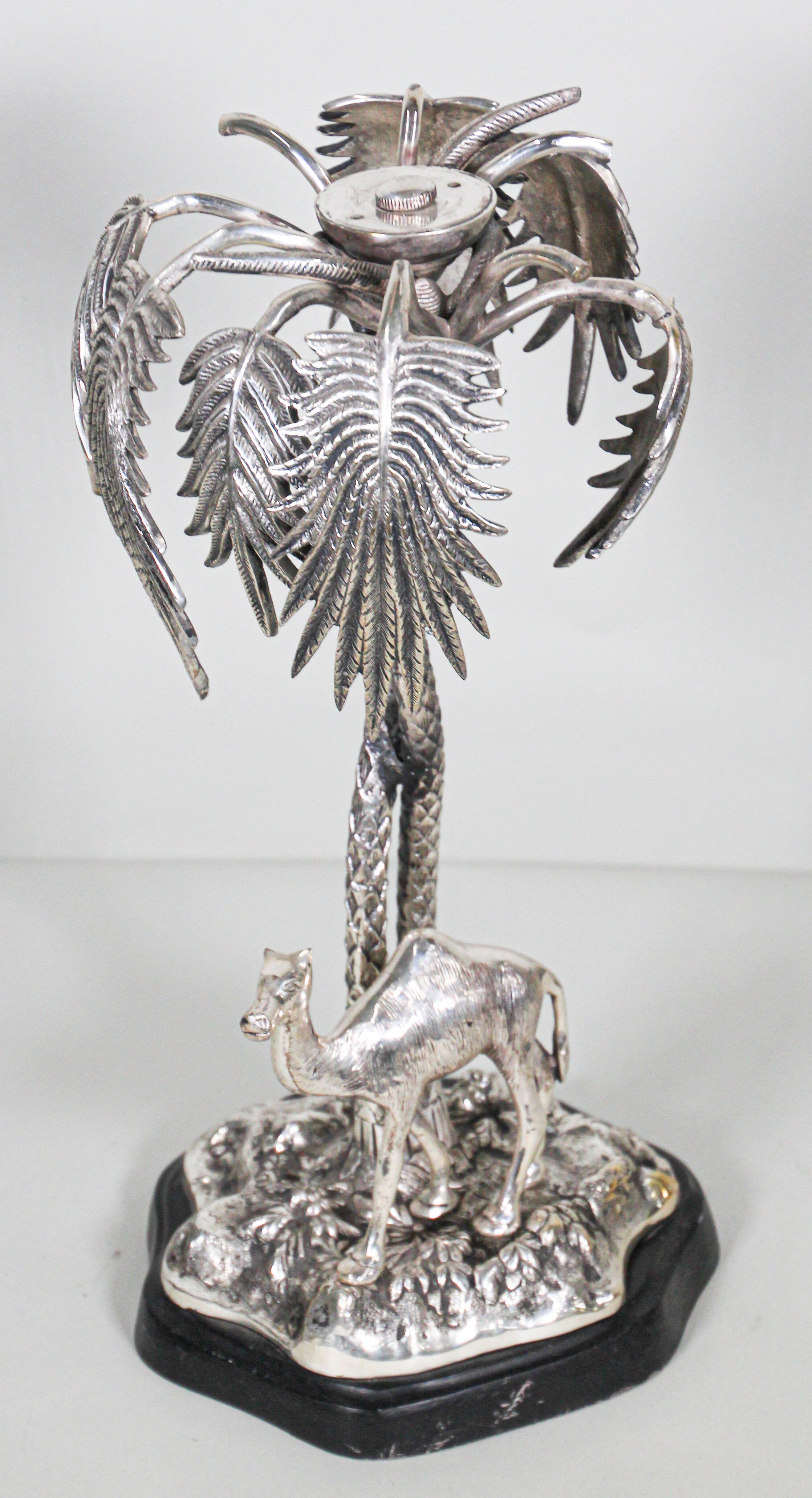 Large cast silver metal color sculpture of a desert scene in the form of two entwined palm trees and a camel standing on a rocky base under the palm trees.
A Victorian continental School 19th century style, Viennese Islamic Orientalist Art.
A black