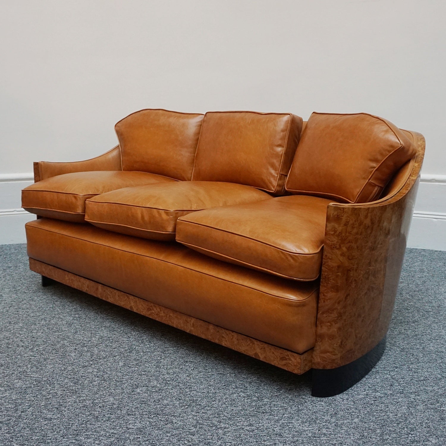Art Deco club sofa by Maurice Adams. Curved wraparound burr walnut veneer with ebonized banding. Re-upholstered in brown leather. Depth measured with and without optional back cushions. 

Dimensions: H 76cm W 169cm D 98cm Seat H 54cm W 150cm D