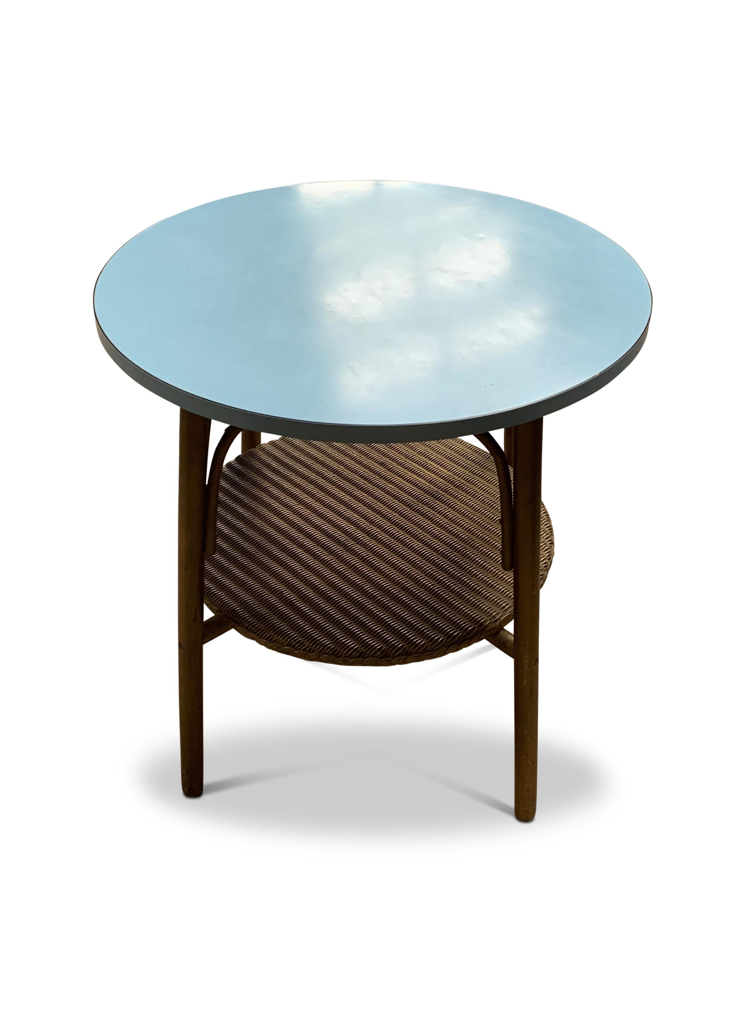 Petite table d'appoint ronde en bois courbé Lloyds des années 1930. Espace de rangement supplémentaire grâce à une petite étagère.

Le plateau de la table a une surface dure bleue, facile à essuyer et à nettoyer. Avec une base tressée en or et des