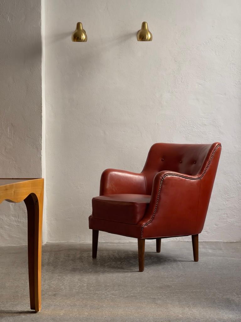 An exquisite 1940s Danish Modern Easy Chair upholstered in luxurious patinated red leather that has aged beautifully over the years. Ornate brass nails adorn the edges, adding a touch of sophistication. Attributed to the renowned  manufacturer Fritz