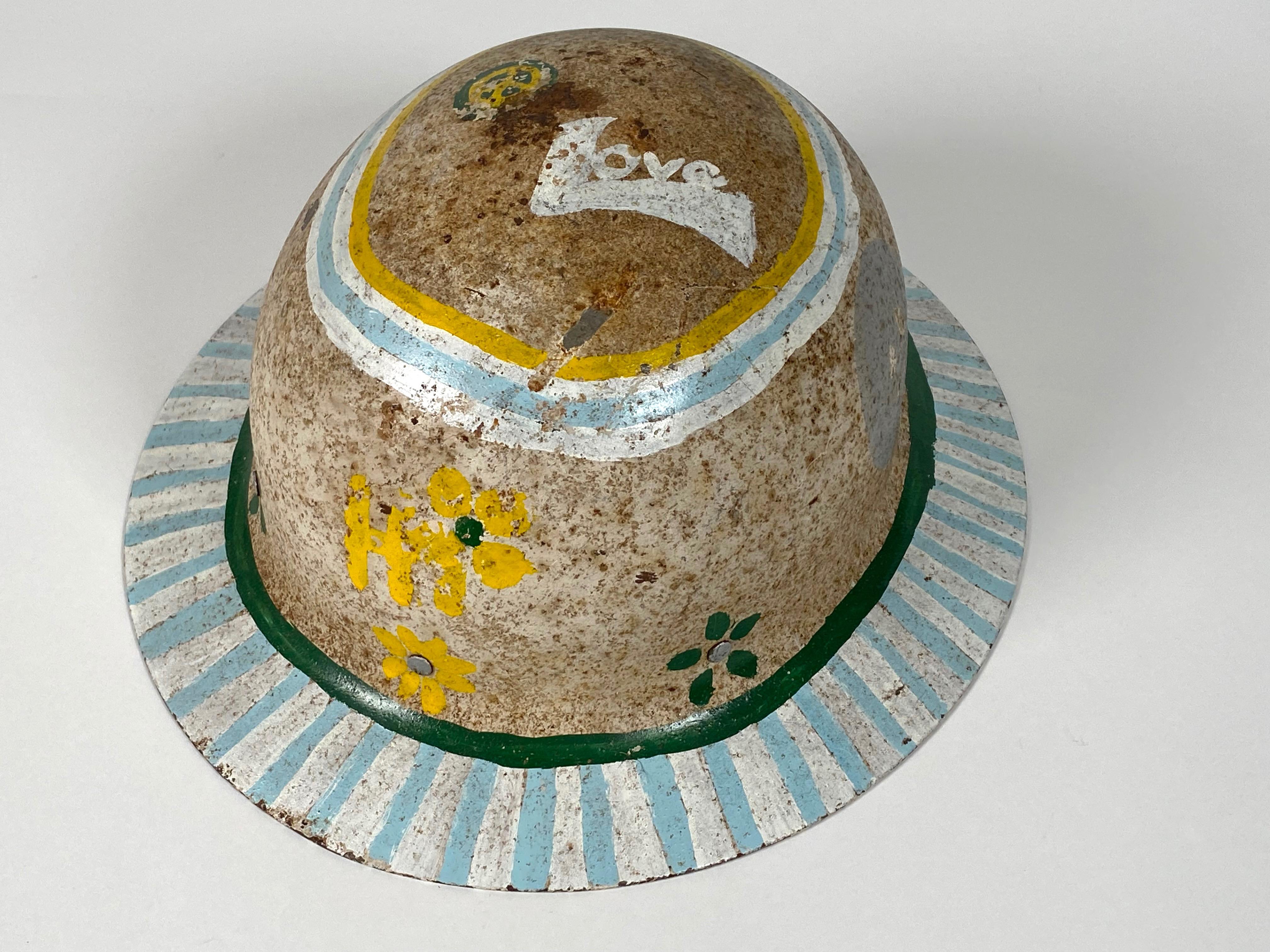 Original 1960s hand painted Hippie hardhat, embellished with Peace Signs, Flowers and the words Peace, Love and Hi. Painted with green, silver, white and pale blue. The brim has contrasting white and blue bands. Patina to the white paint with