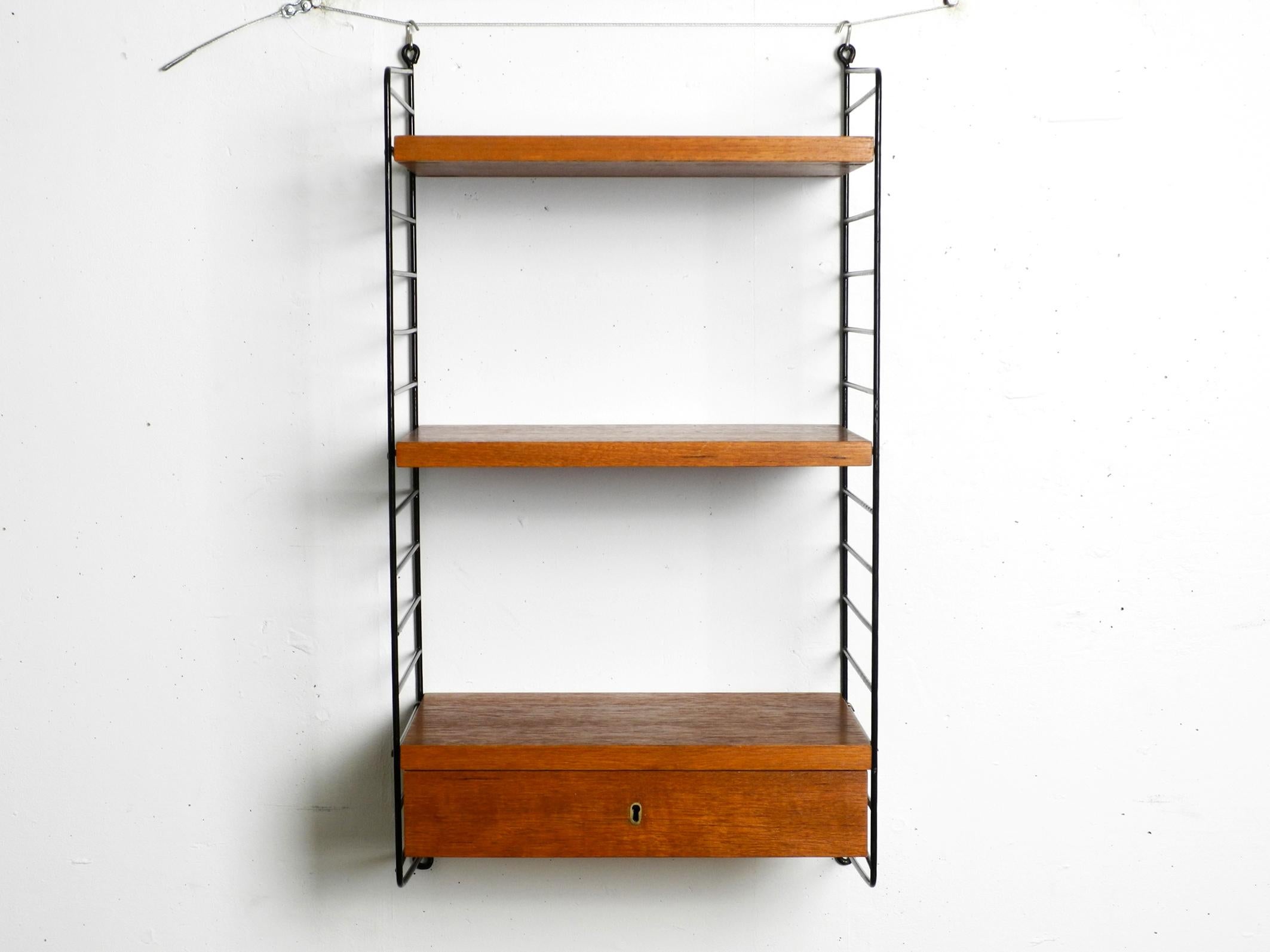 Narrow original 60s Nisse Strinning String teak wall shelf. 
Made in Sweden. 
Two ladders with shelfs and one drawer with a depth of 30cm. 
All wooden parts are covered with teak veneer.
Very clean with few normal signs of use.
All ladders are in