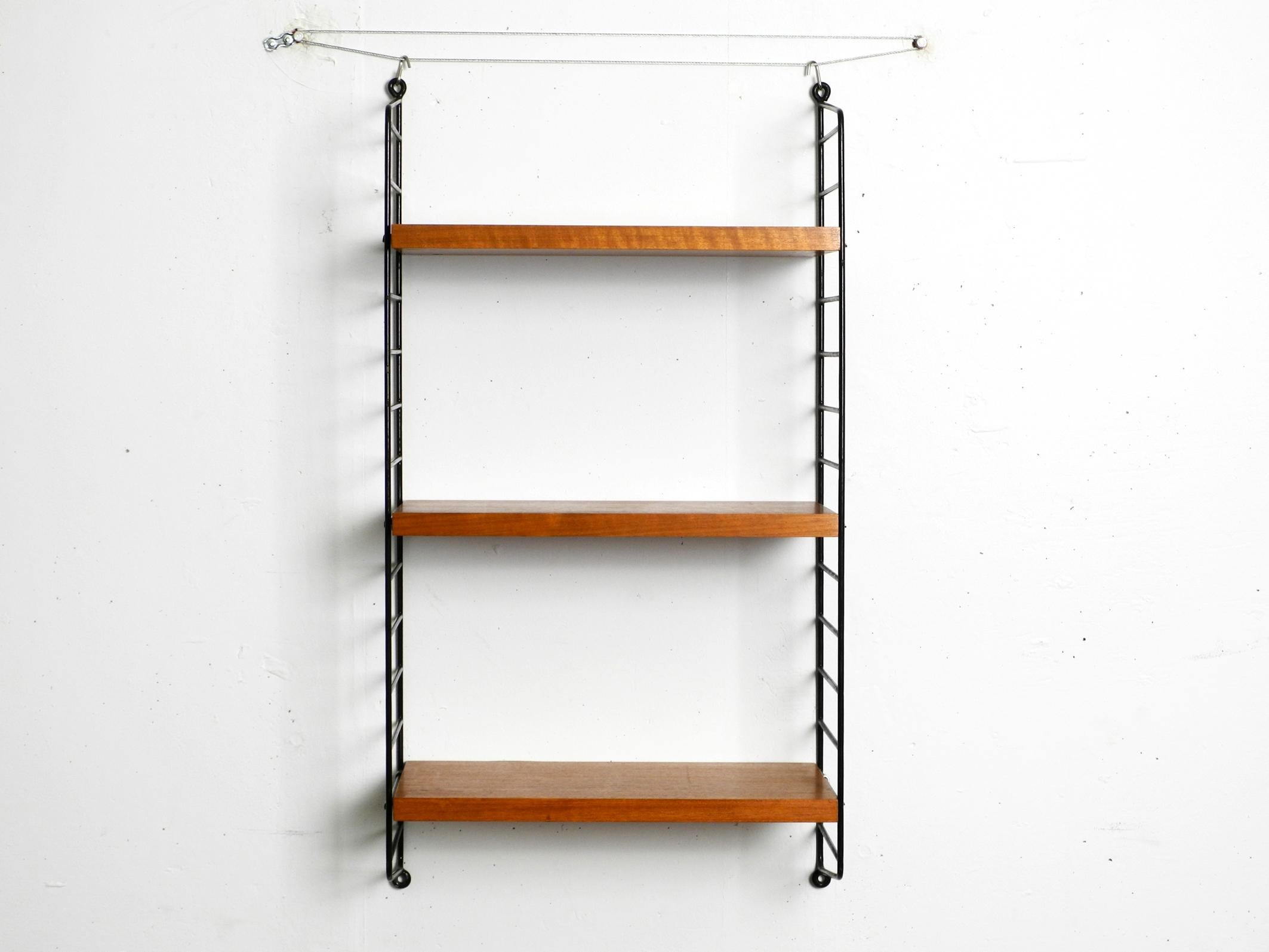 Original 60s Nisse Strinning wall hanging shelf with three solid wood shelves with teak veneer.
2 metal ladders with black plastic coating.
All four ladders are well preserved. The plastic coating is still good.
The casing is scratched at the holes