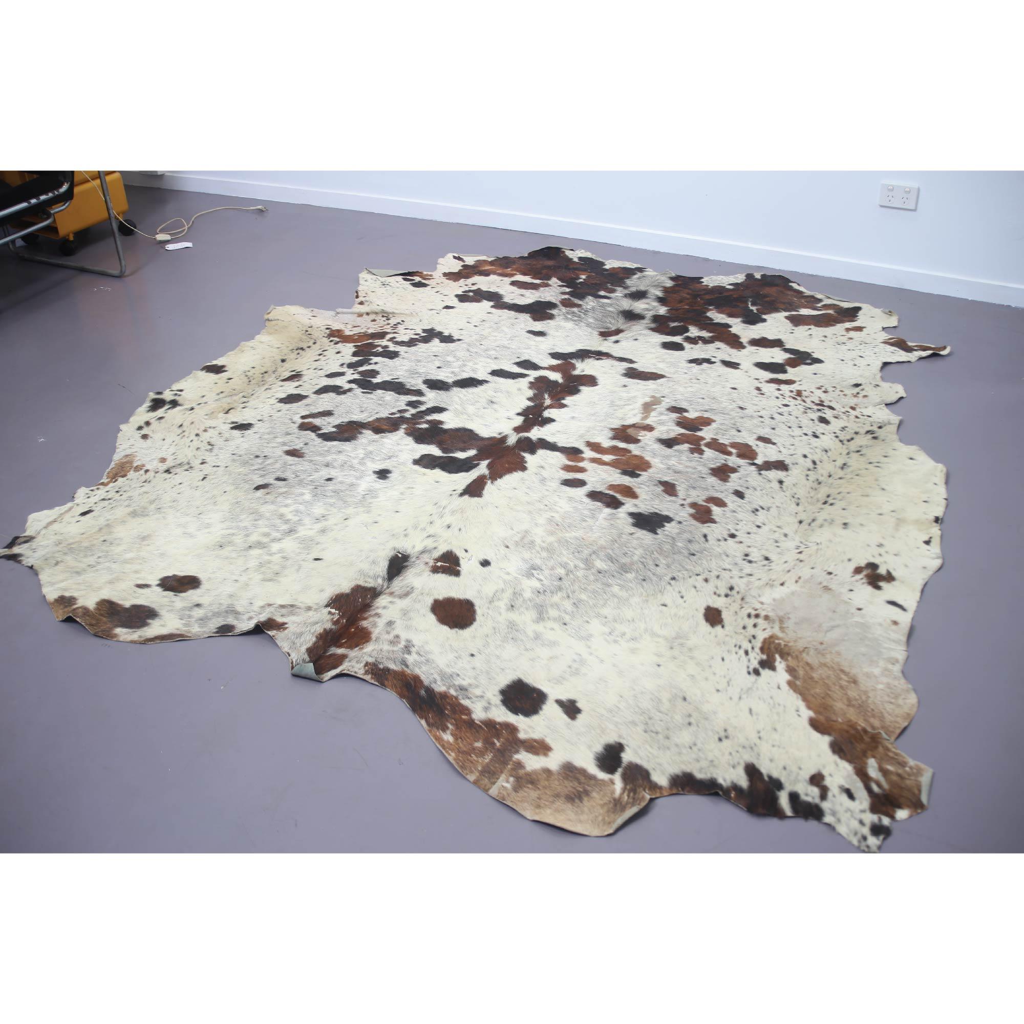 Natural cow hide rug, spotted tri-color with white, brown and black speckles.