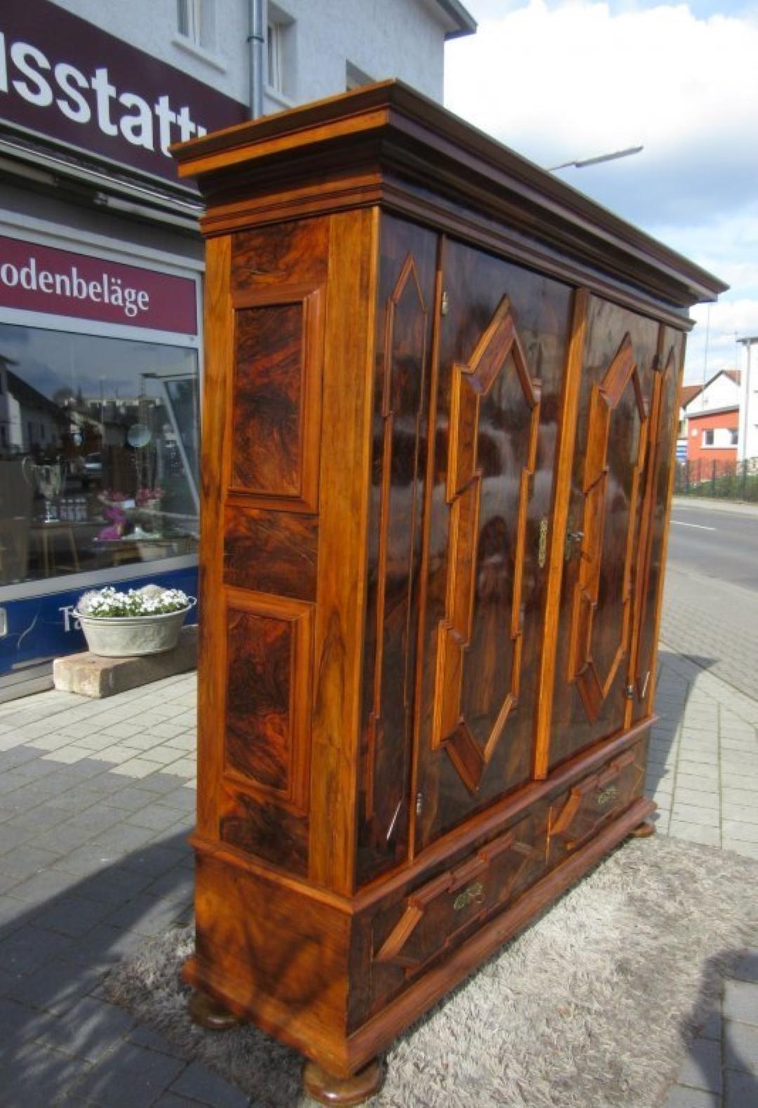 Amazing one of a kind baroque armoire cabinet with a stunning and luxurious dark walnut veneer. This amazing piece of antique furniture convinces with its wonderful wooden color and graining. Features geometrically carved patterns on the doors and