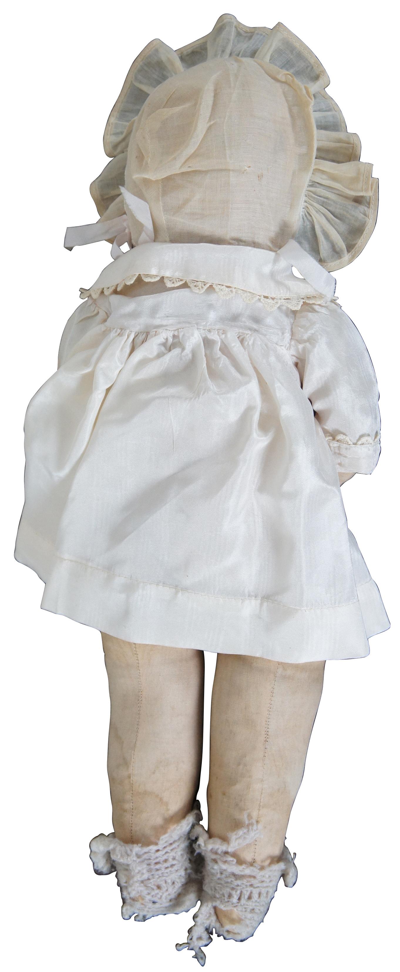 Early 20th century Kathe Kruse painted cloth baby doll with blonde hair and brown eyes, dressed in a white outfit with bonnet and knit socks.“Käthe Kruse, born Katharina Simon (17 September 1883 in Dambrau-19 July 1968 in Murnau am Staffelsee) was a