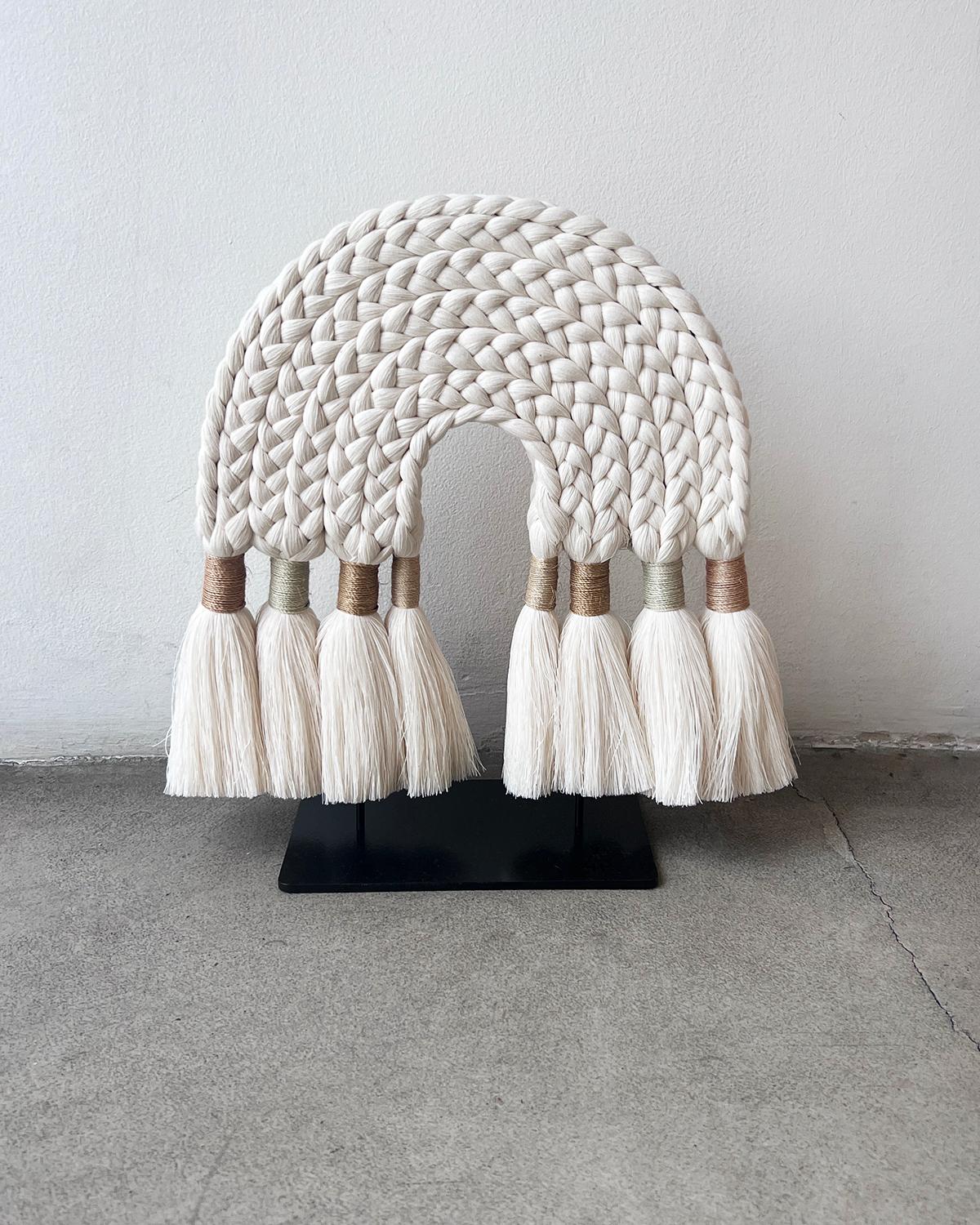 Questa bellissima scultura presenta un arco realizzato con un filo di cotone grezzo intrecciato con nappe legate con fibre di sansevieria siena color malva, blu e bruciato alle estremità. Si trova su un supporto in metallo zincato. È perfetto per