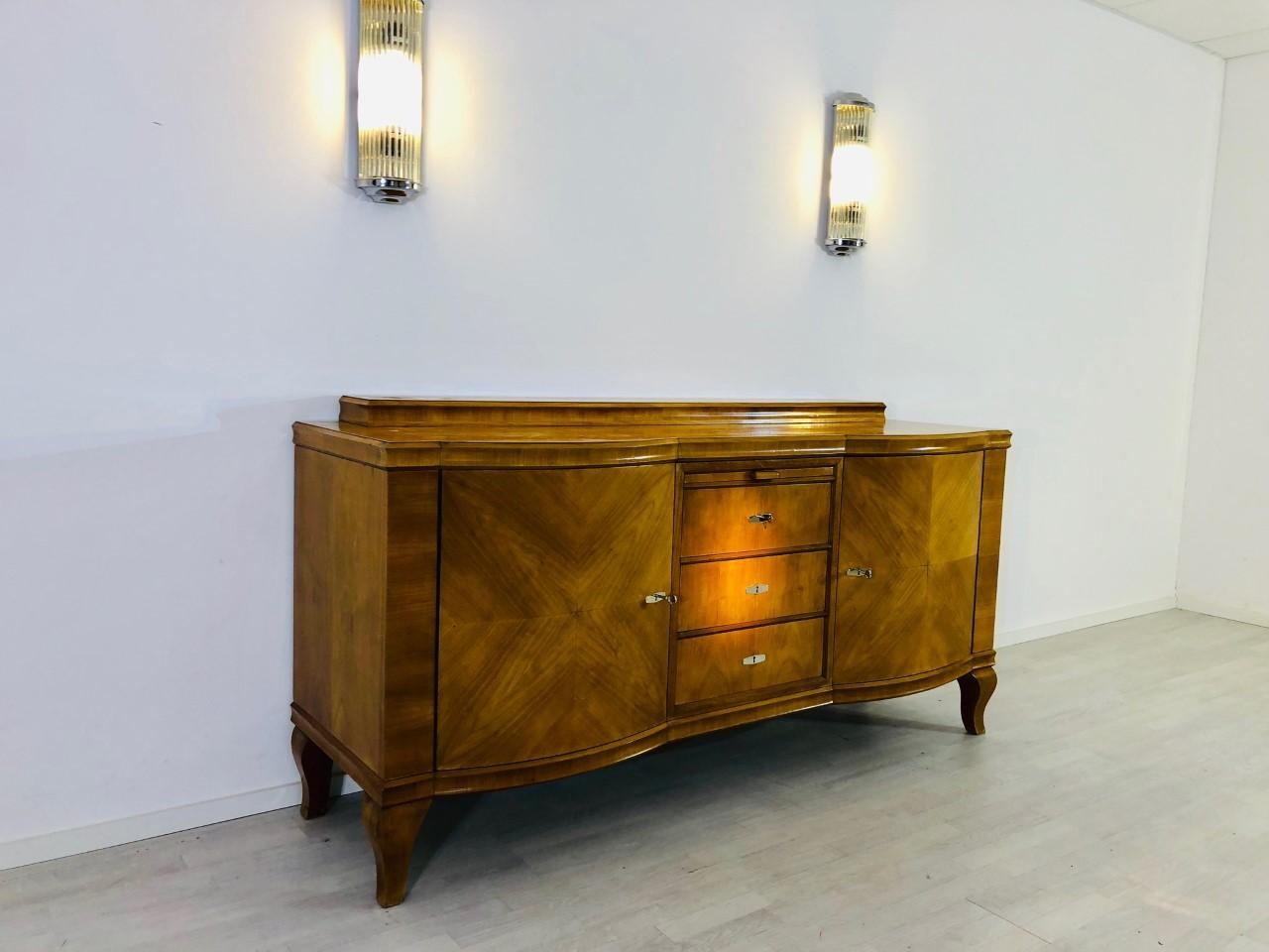 Original Art Deco sideboard or buffet from the 1920s. Veneered with a luxurious grained walnut wood with a beautiful, yellow gold color. Convinces with its unique Art Deco design, with wonderfully carved French feet and a hutch on the top plate. The